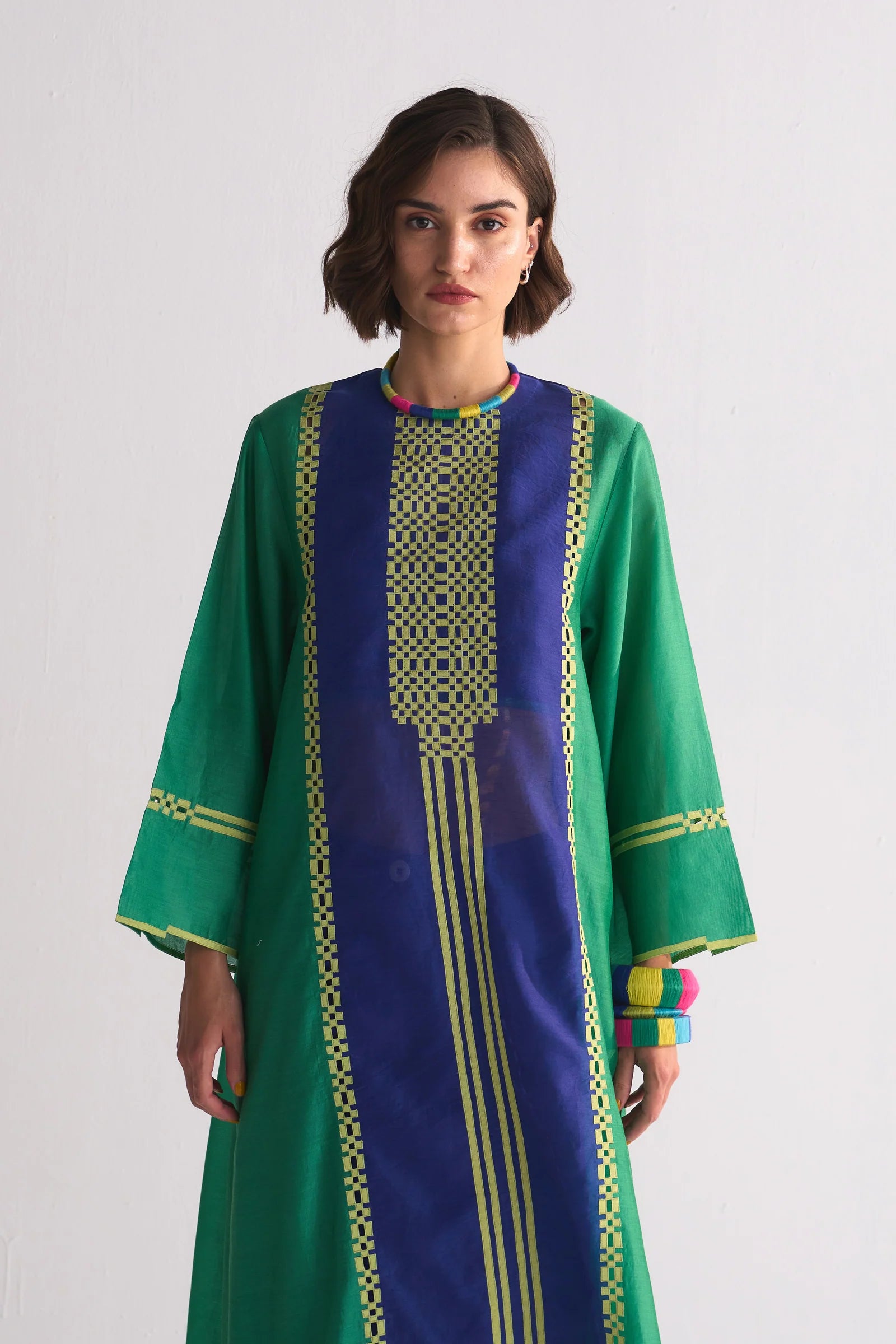 Woman wearing a green and blue dress with intricate patterns on a white background