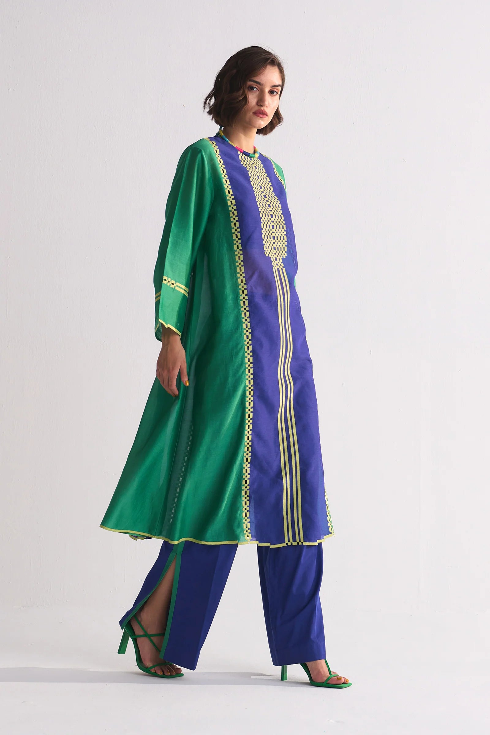 A model in a green and navy blue colour-blocked kameez featuring yellow geometric hand-cut appliqué and vertical stripe details.