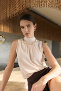 Woman wearing a beige sleeveless top with a gold necklace in an indoor setting