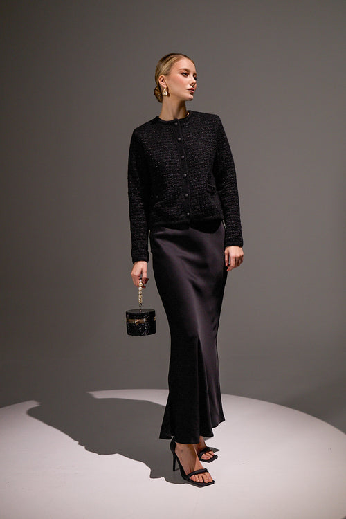 Woman in a black outfit holding a small black handbag against a gray background