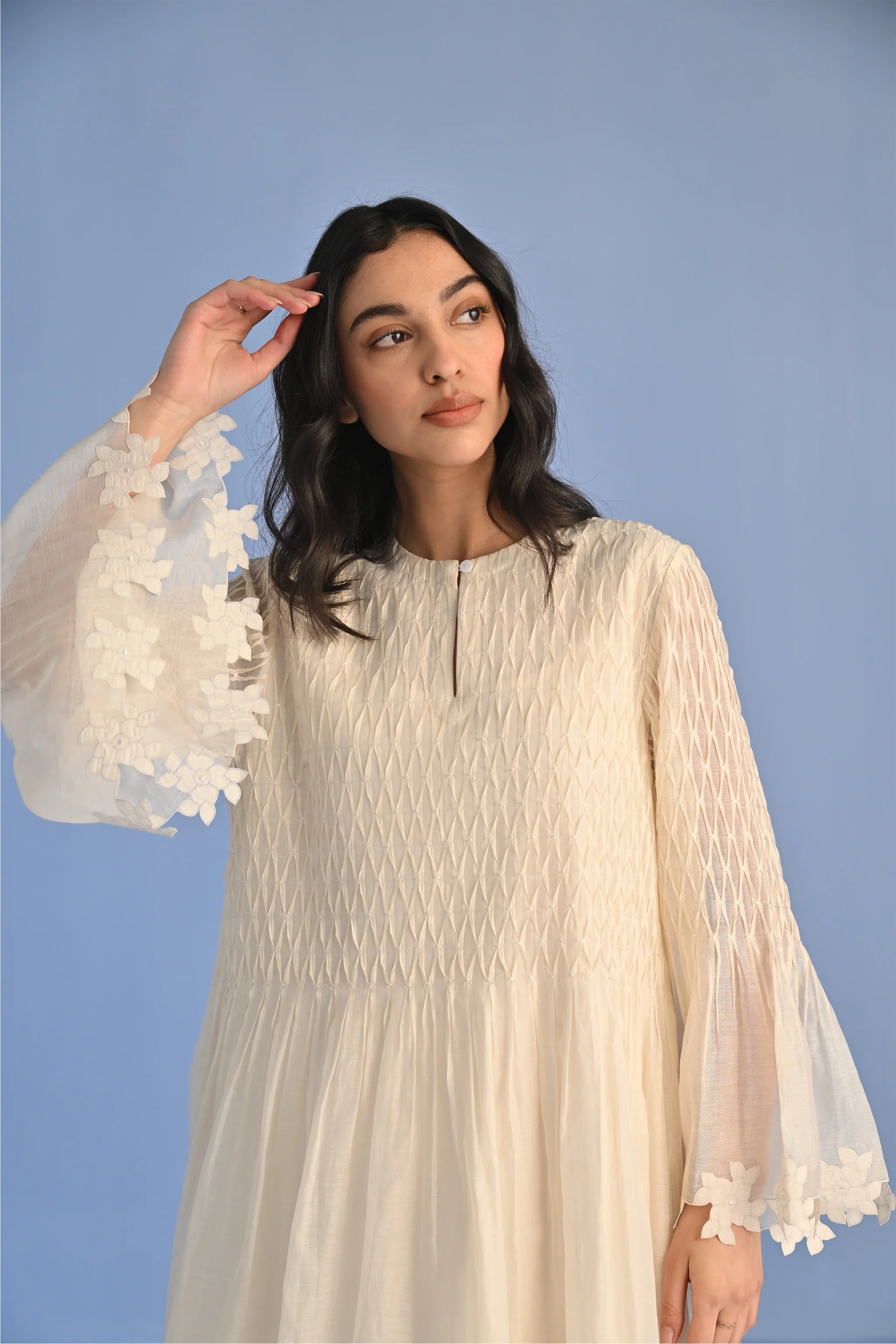 A floor-length ivory Cotton Silk Chanderi dress with a pleated skirt, featuring intricate geometric cutwork panels on the bodice and hemline.