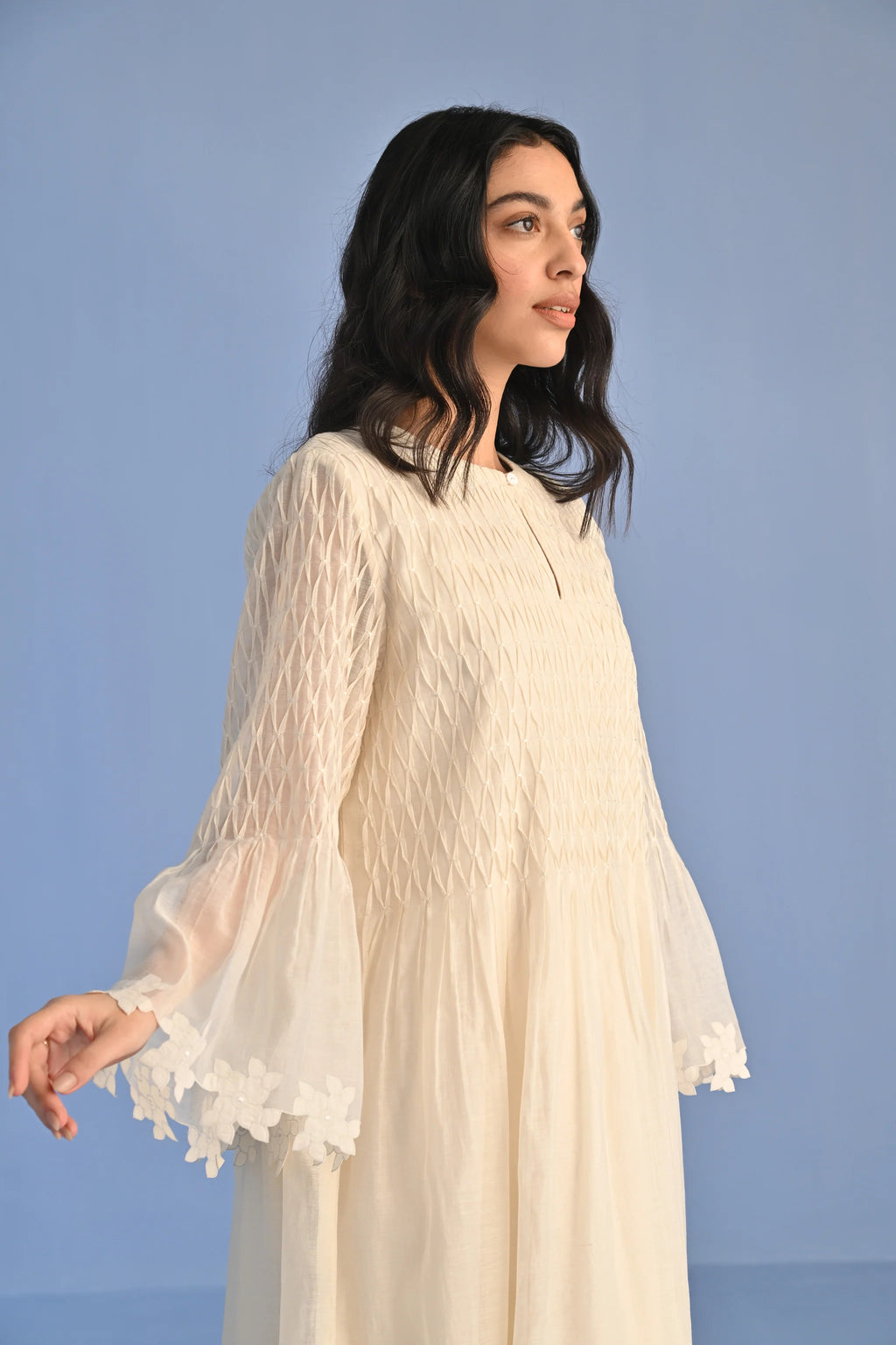 A floor-length ivory Cotton Silk Chanderi dress with a pleated skirt, featuring intricate geometric cutwork panels on the bodice and hemline.