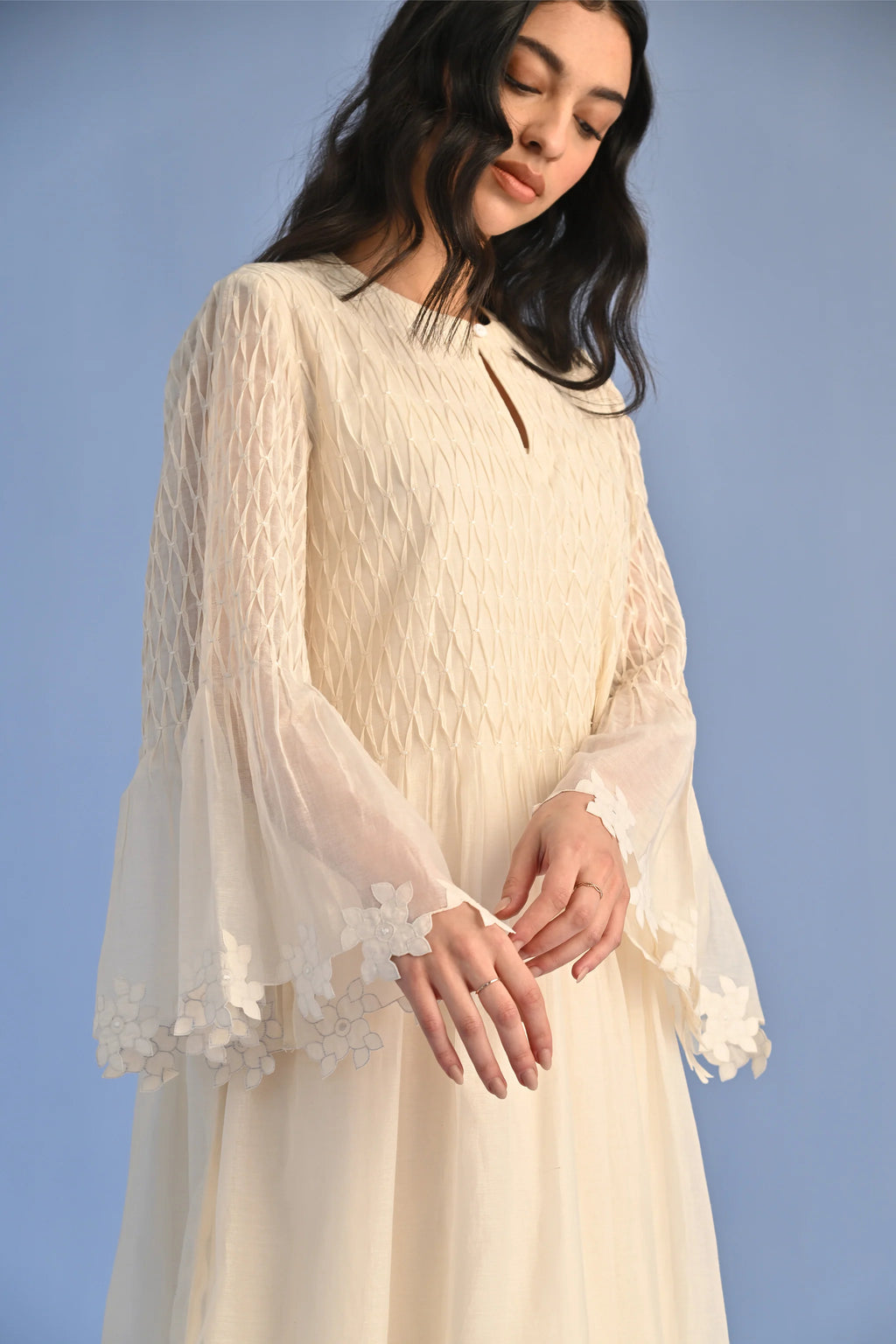 A floor-length ivory Cotton Silk Chanderi dress with a pleated skirt, featuring intricate geometric cutwork panels on the bodice and hemline.