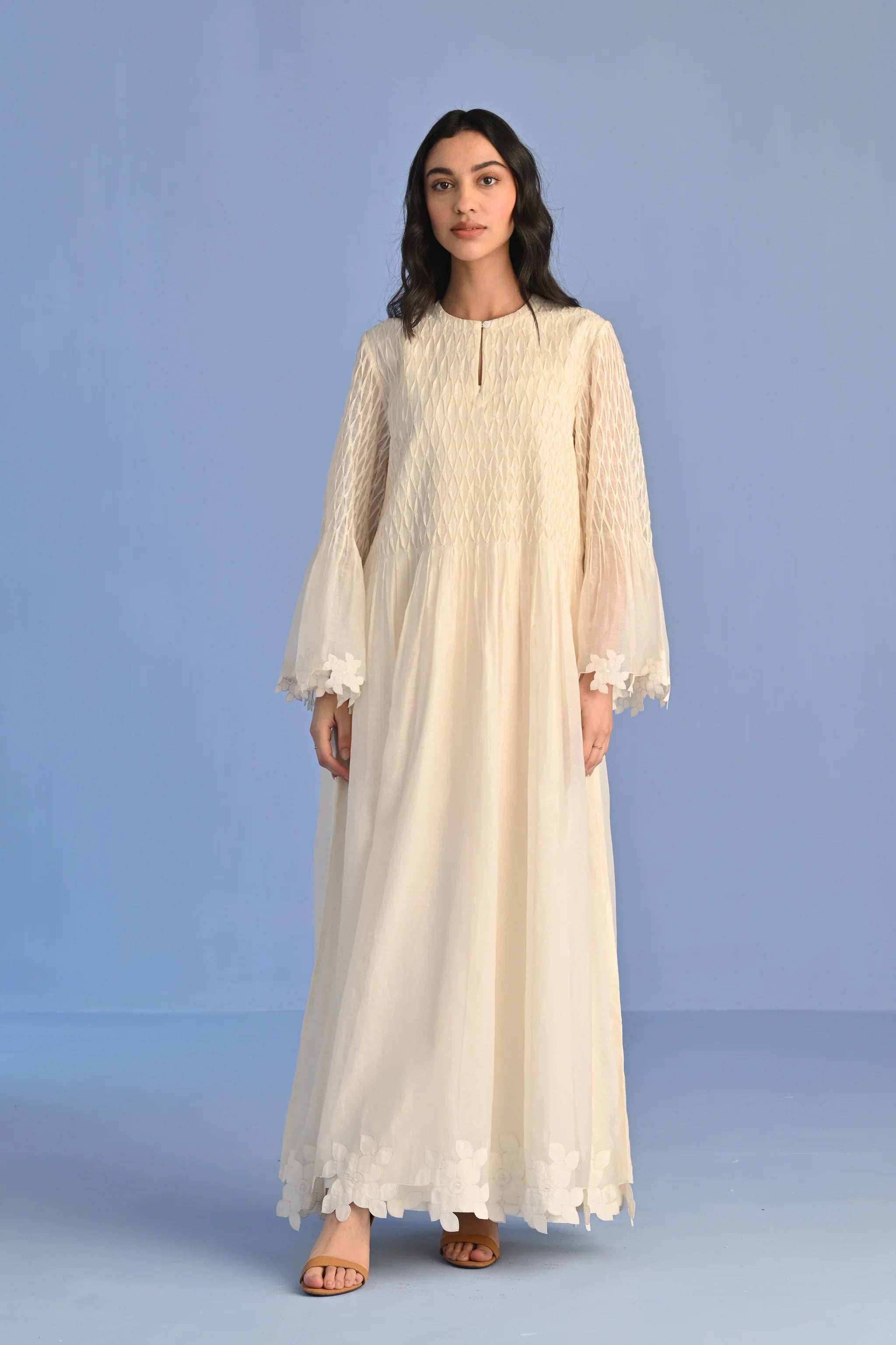A floor-length ivory Cotton Silk Chanderi dress with a pleated skirt, featuring intricate geometric cutwork panels on the bodice and hemline.