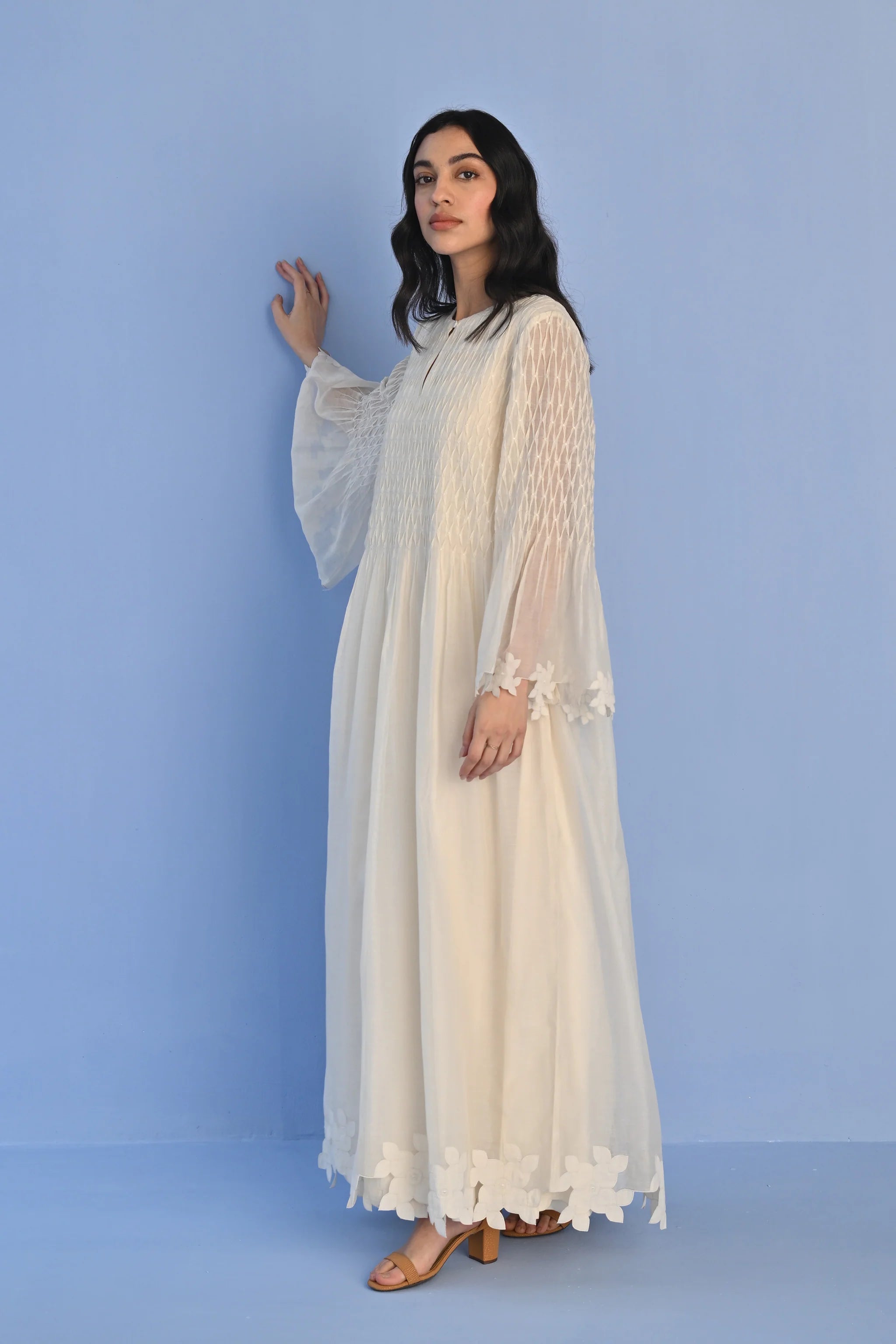A floor-length ivory Cotton Silk Chanderi dress with a pleated skirt, featuring intricate geometric cutwork panels on the bodice and hemline.