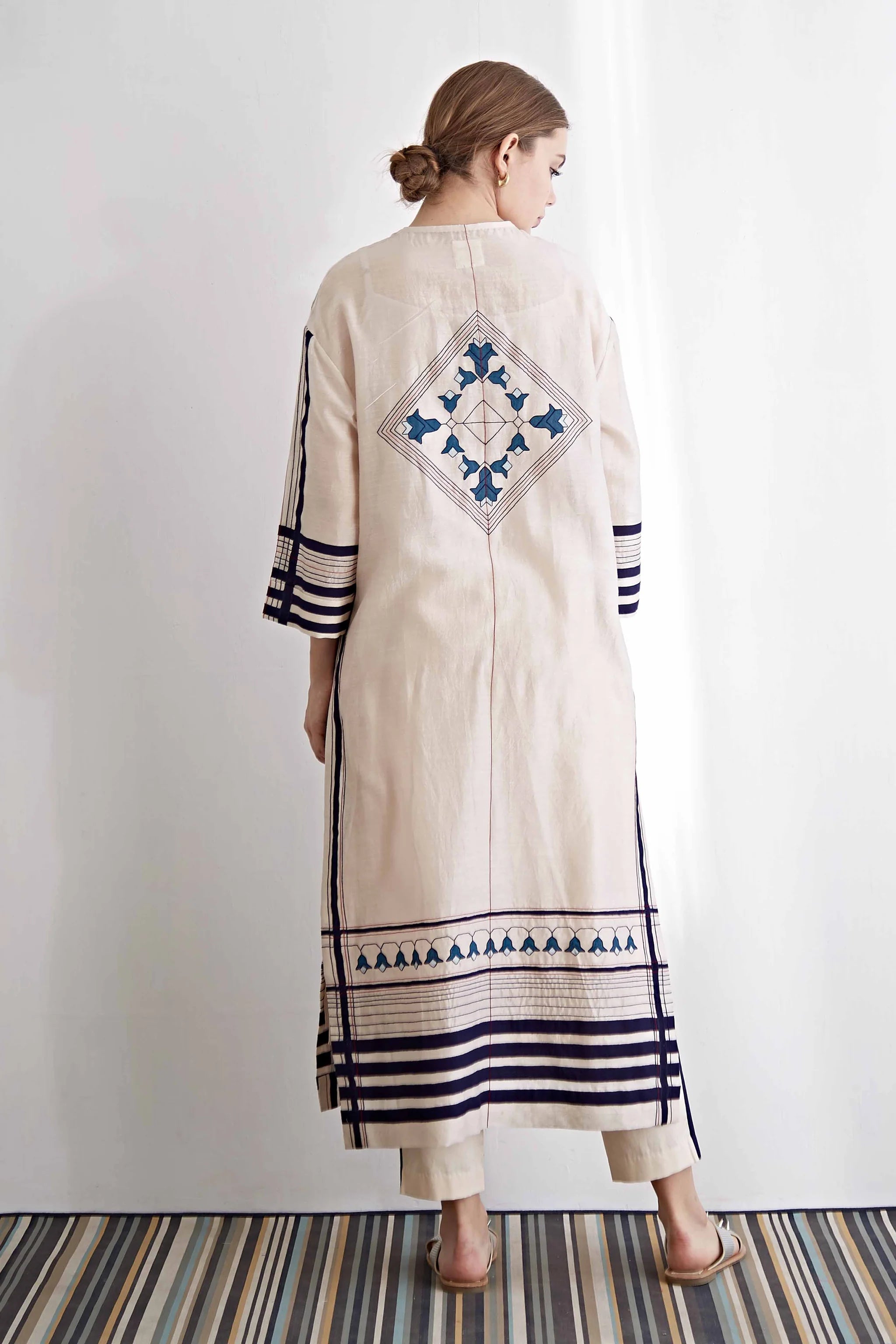 Woman wearing a long, cream-colored dress with blue patterns and stripes on a white background