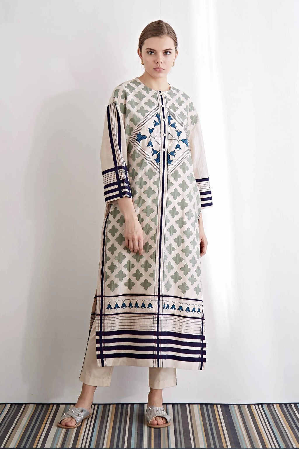 An oversized ivory drop-shoulder kameez featuring blue and green geometric hand-cut appliqué motifs and horizontal striped borders.
