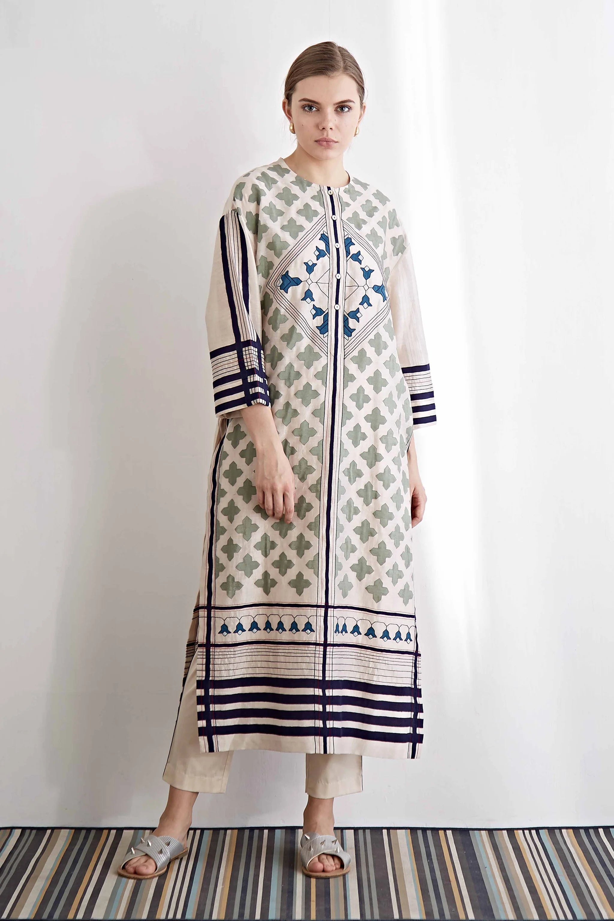 An oversized ivory drop-shoulder kameez featuring blue and green geometric hand-cut appliqué motifs and horizontal striped borders.