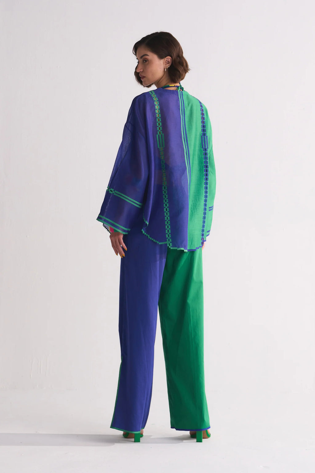 A model in a round-hem indigo Chanderi shirt with green colour-blocked panels and geometric hand-cut appliqué along the hem and shoulders.