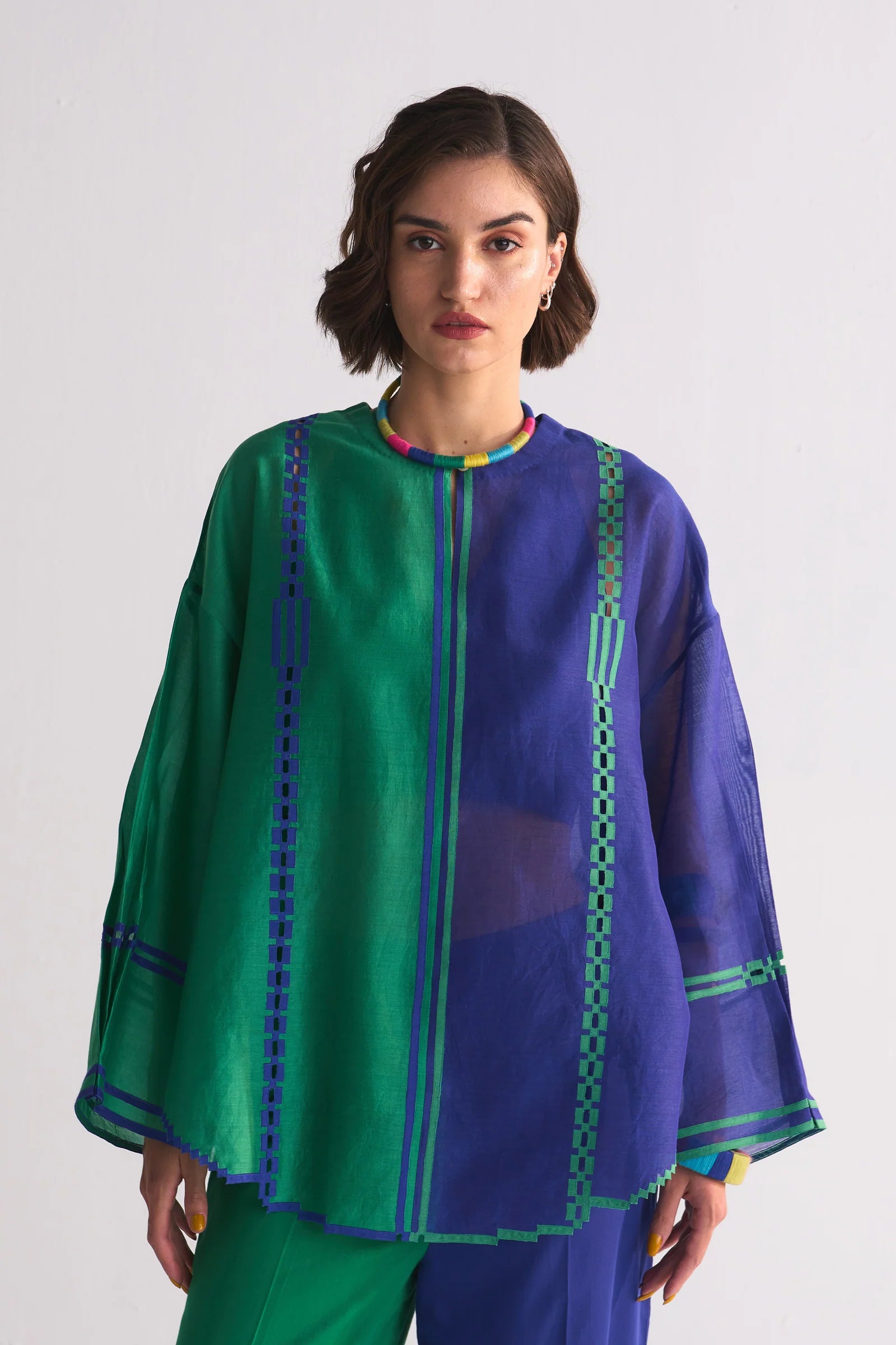 A model in a round-hem indigo Chanderi shirt with green colour-blocked panels and geometric hand-cut appliqué along the hem and shoulders.