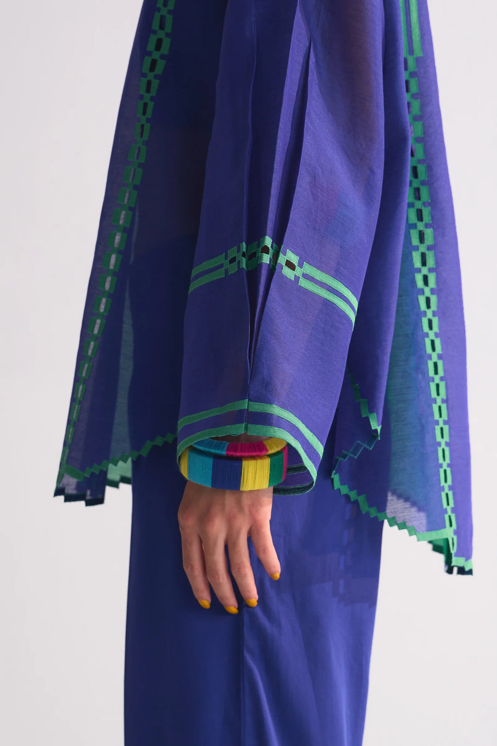 A model in a round-hem indigo Chanderi shirt with green colour-blocked panels and geometric hand-cut appliqué along the hem and shoulders.