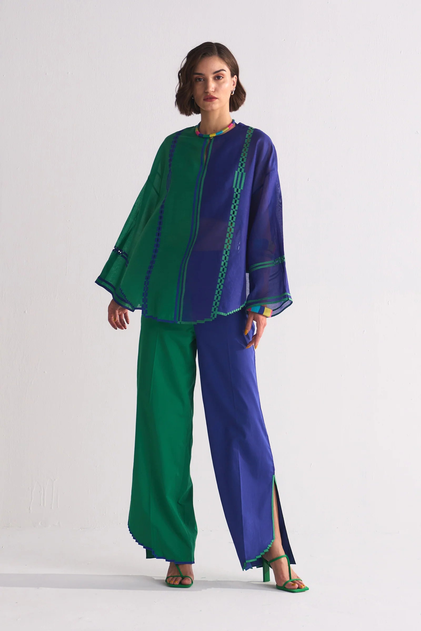 A model in a round-hem indigo Chanderi shirt with green colour-blocked panels and geometric hand-cut appliqué along the hem and shoulders.
