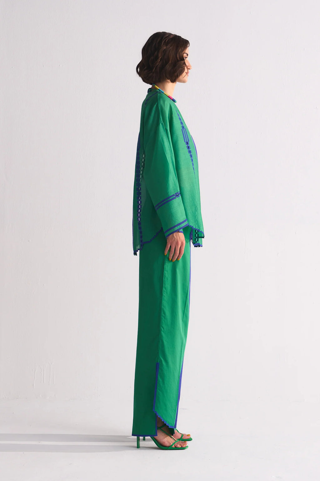 A model in a round-hem indigo Chanderi shirt with green colour-blocked panels and geometric hand-cut appliqué along the hem and shoulders.