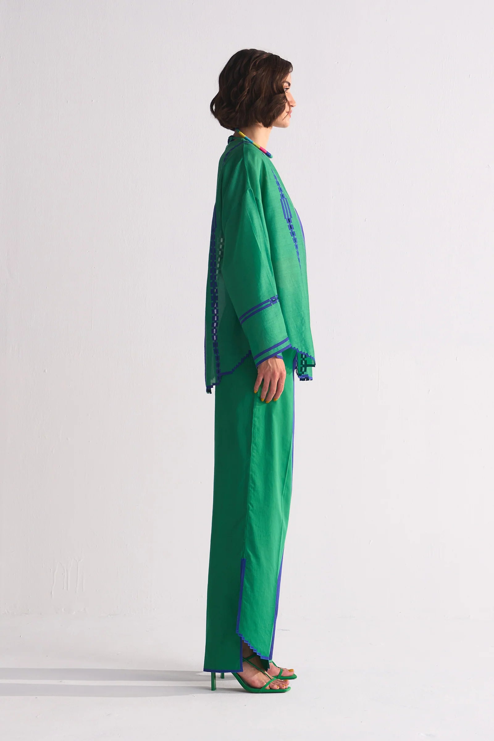 A model in a round-hem indigo Chanderi shirt with green colour-blocked panels and geometric hand-cut appliqué along the hem and shoulders.