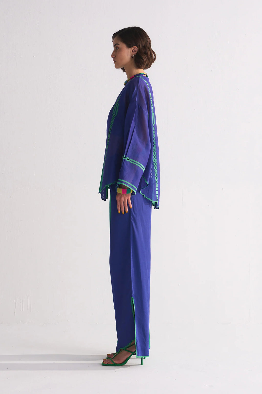 A model in a round-hem indigo Chanderi shirt with green colour-blocked panels and geometric hand-cut appliqué along the hem and shoulders.