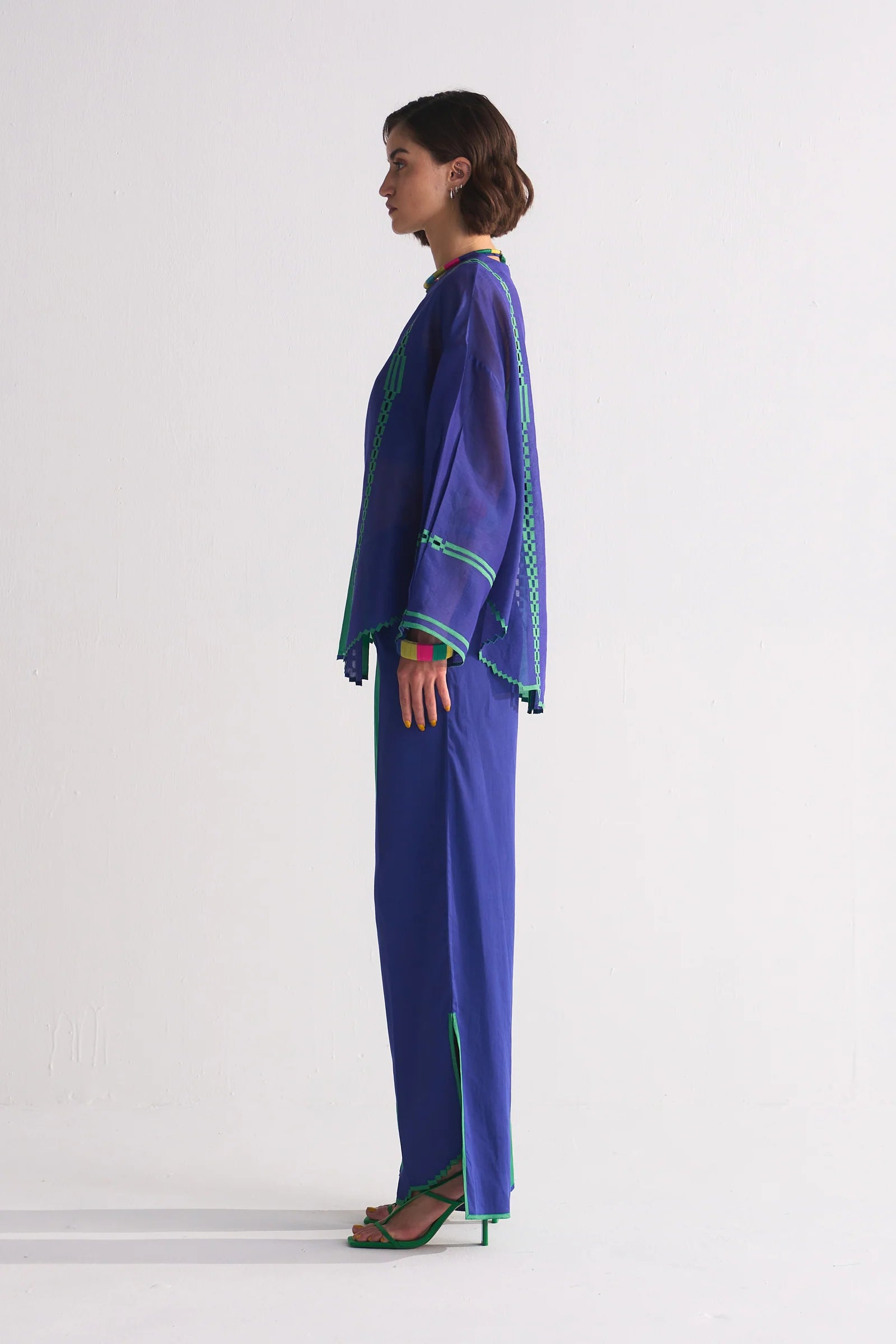 A model in a round-hem indigo Chanderi shirt with green colour-blocked panels and geometric hand-cut appliqué along the hem and shoulders.