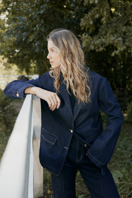 Woman wearing a navy blue blazer standing outdoors with greenery in the background