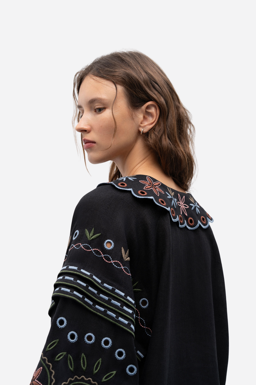 Woman wearing a black sweater with colorful embroidery on a white background