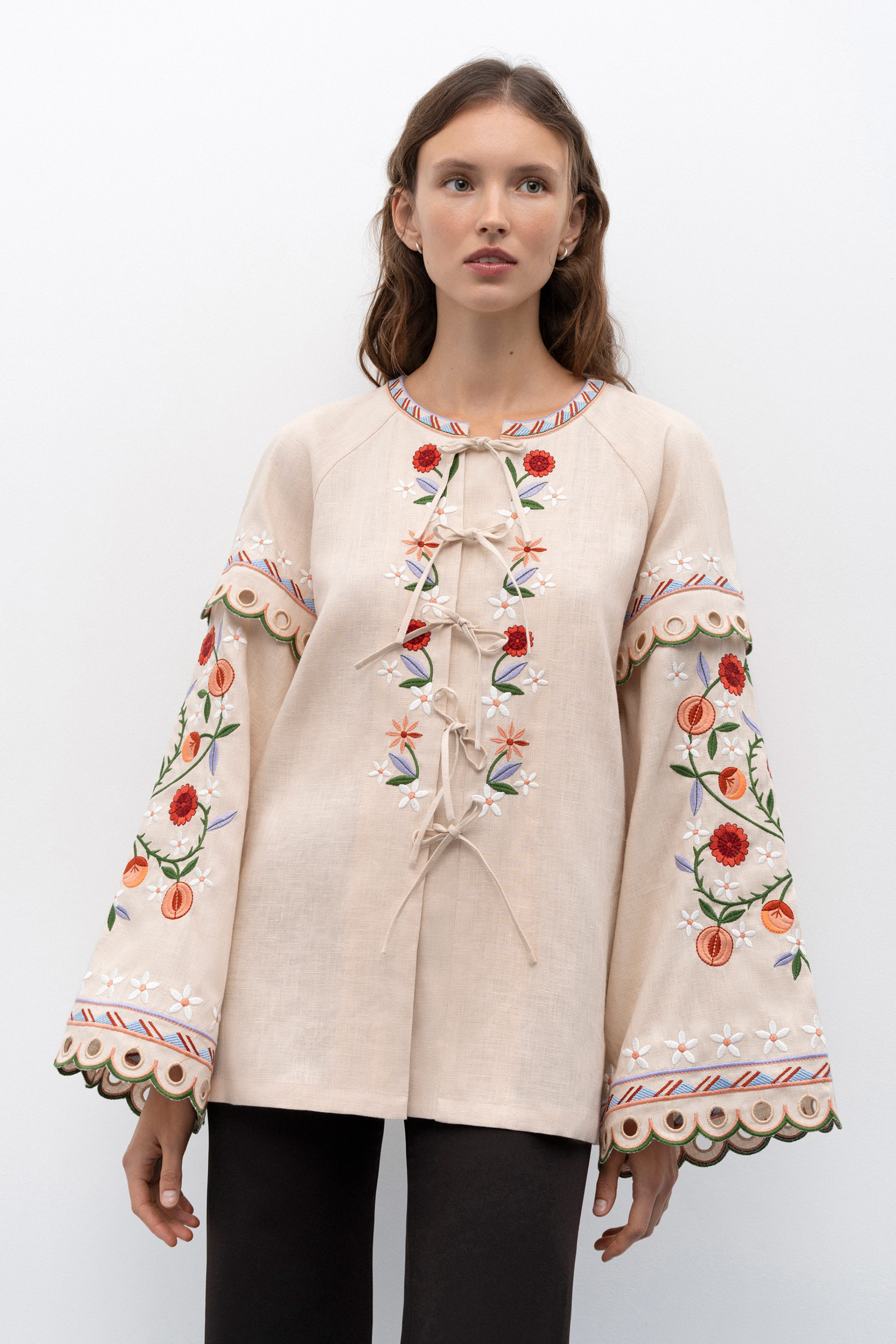 Woman wearing a beige blouse with black floral patterns and blue jeans against a white background