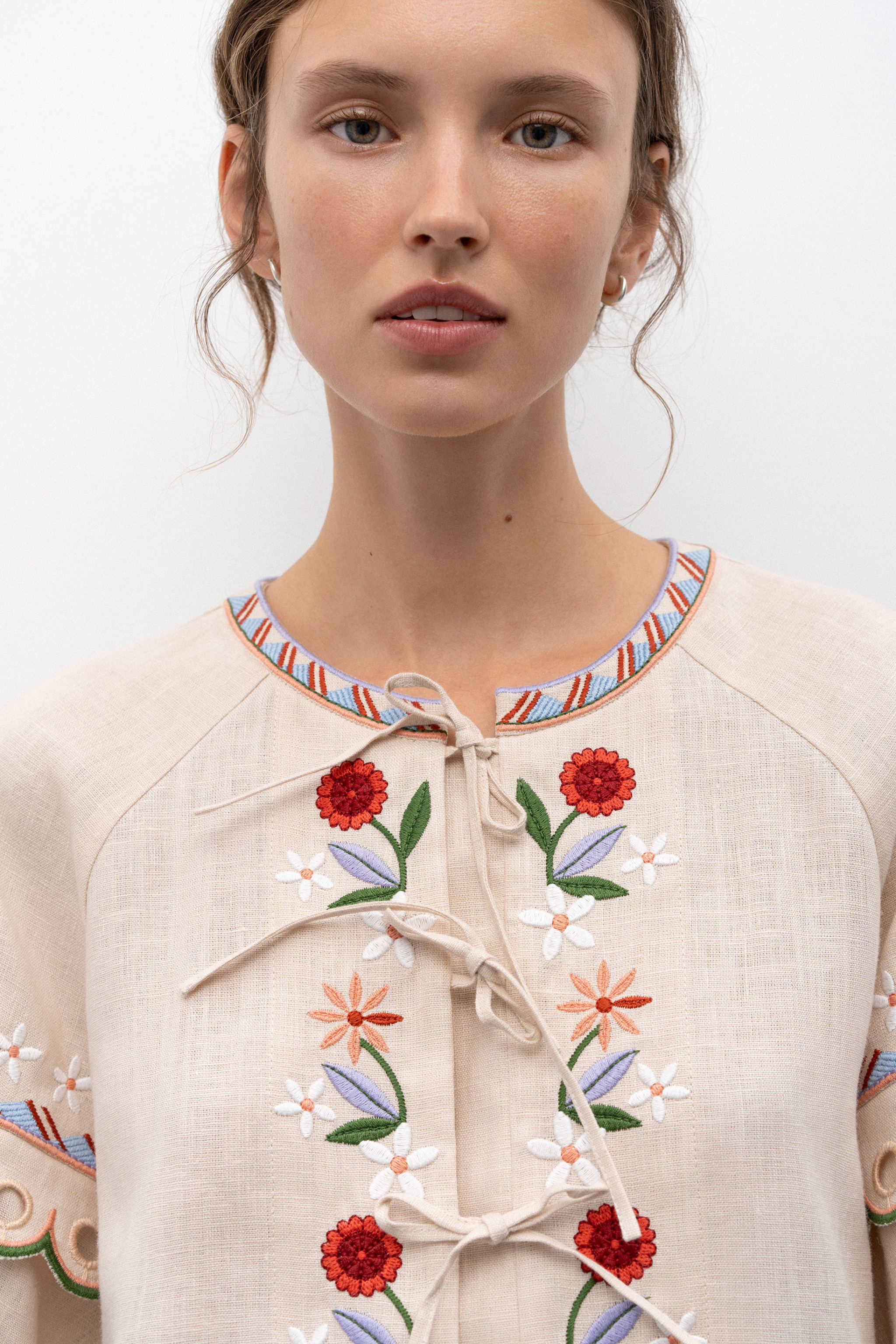 Close-up of a person wearing a beige jacket with black floral patterns on a white background