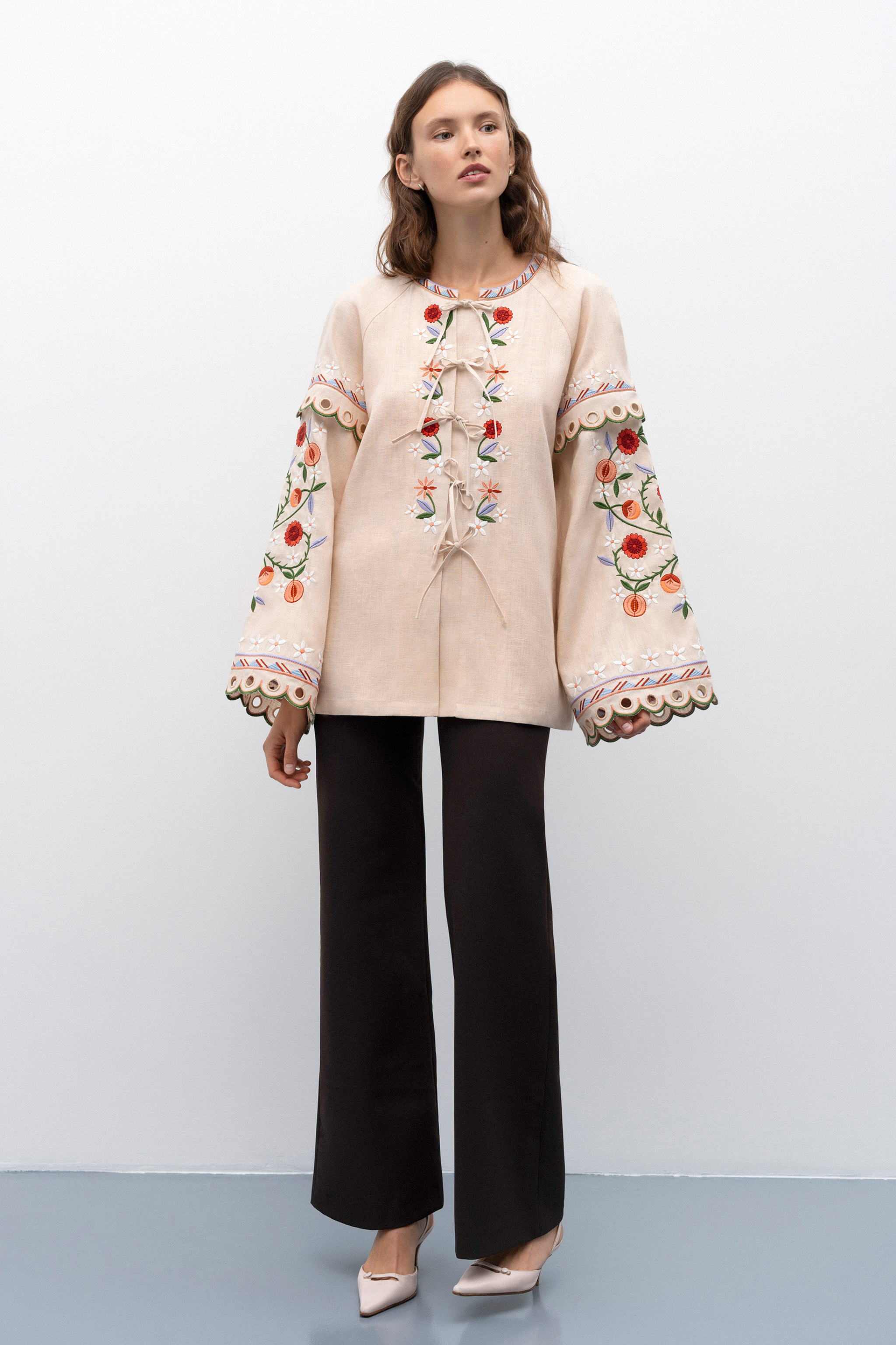 Woman wearing a patterned blouse and blue jeans against a white background