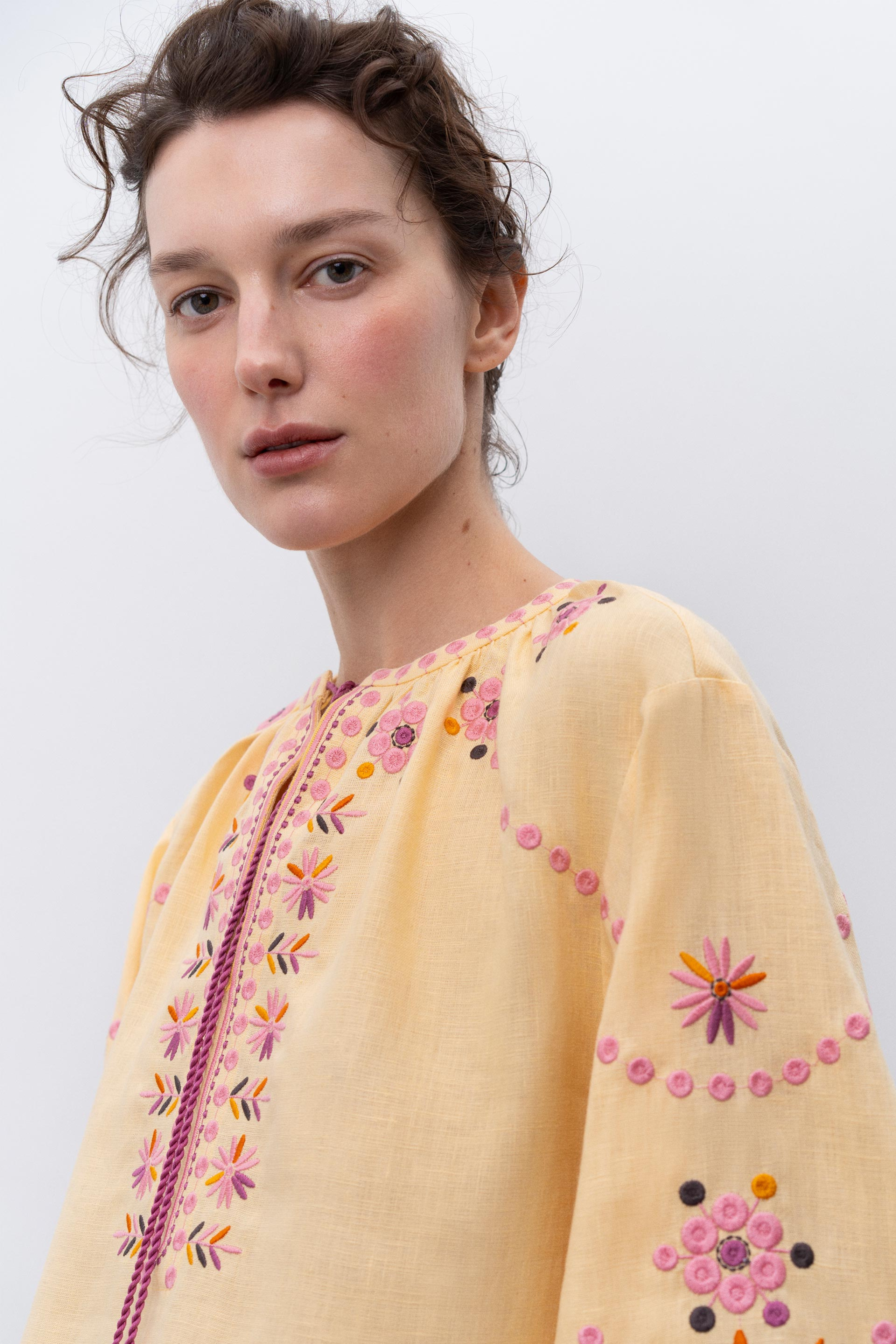 Woman wearing a light yellow blouse with floral embroidery on a white background