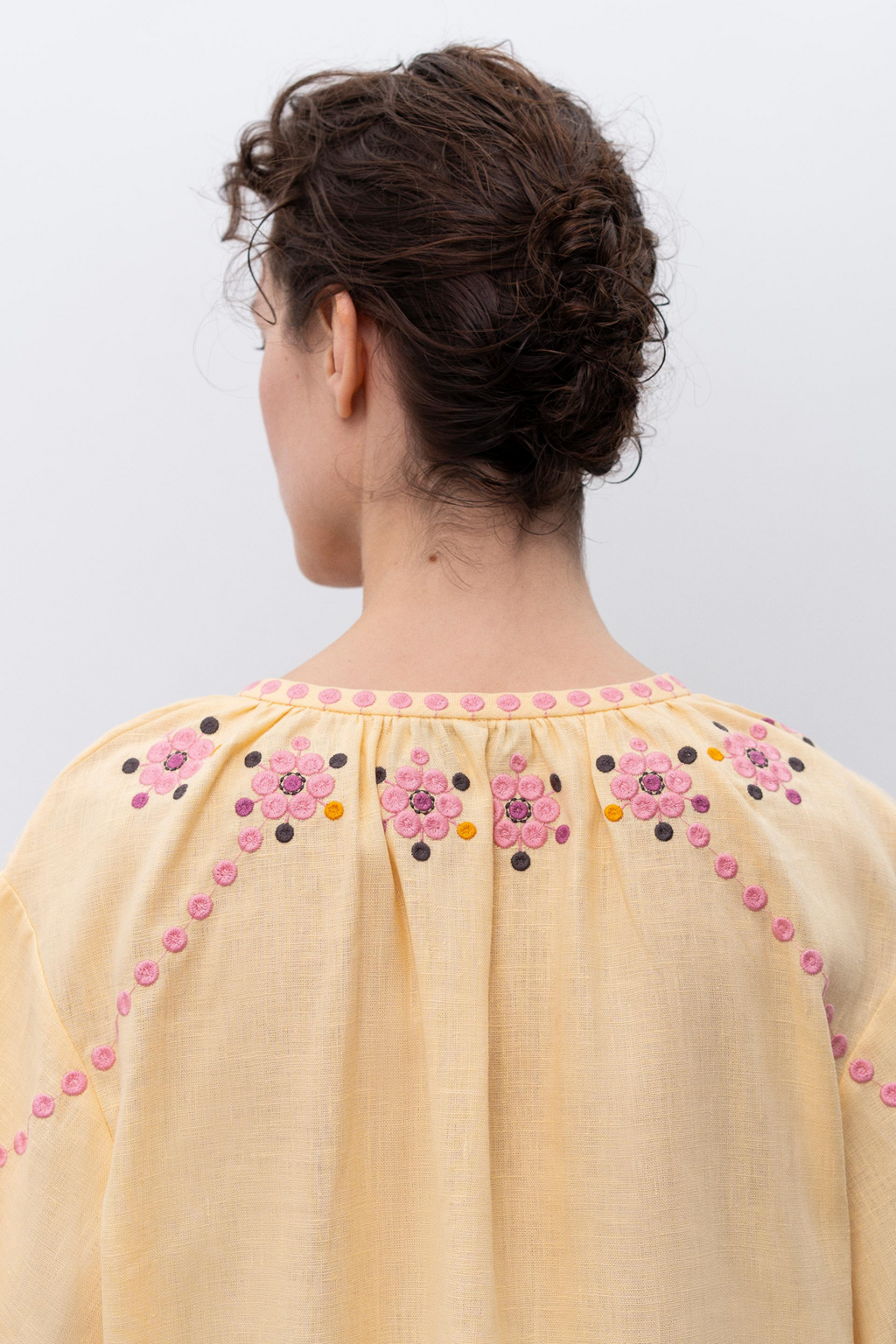 Woman wearing a light yellow blouse with floral embroidery on a white background