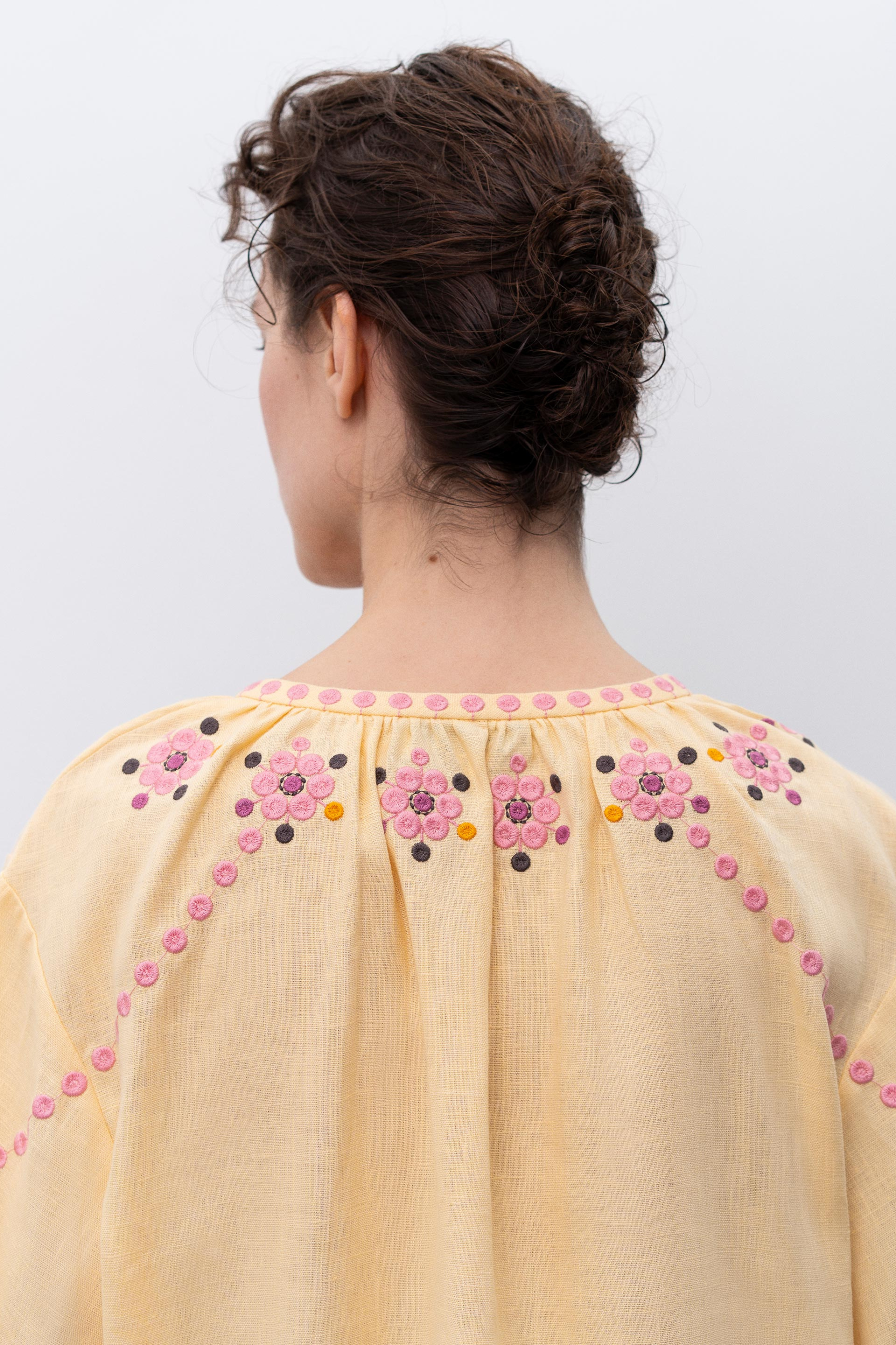 Woman wearing a light yellow blouse with floral embroidery on a white background