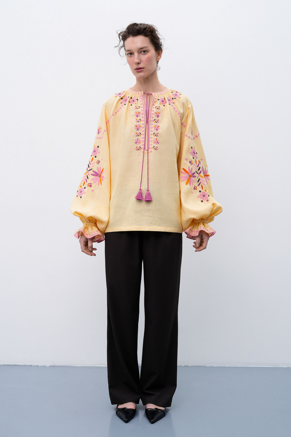 Woman wearing a light yellow blouse with floral embroidery on a white background