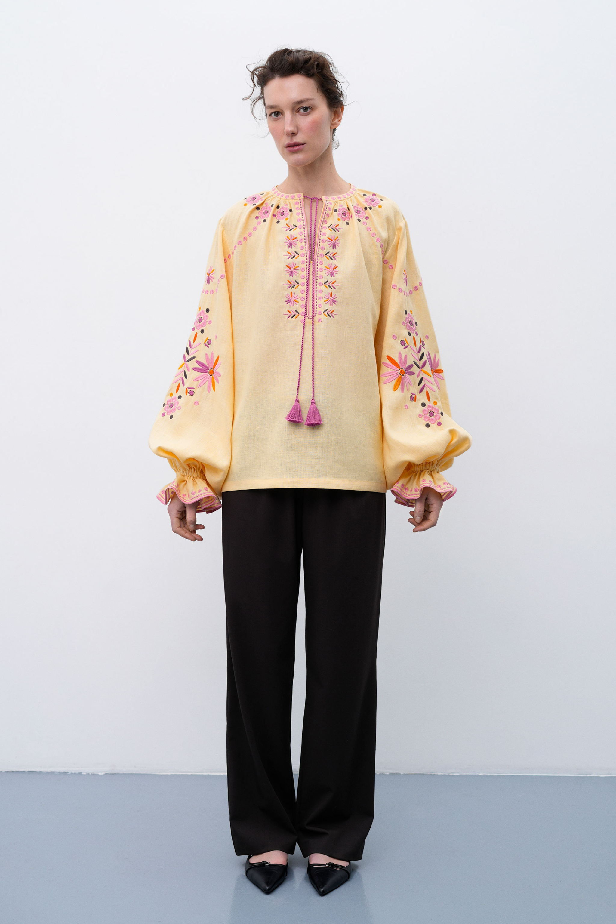Woman wearing a light yellow blouse with floral embroidery on a white background
