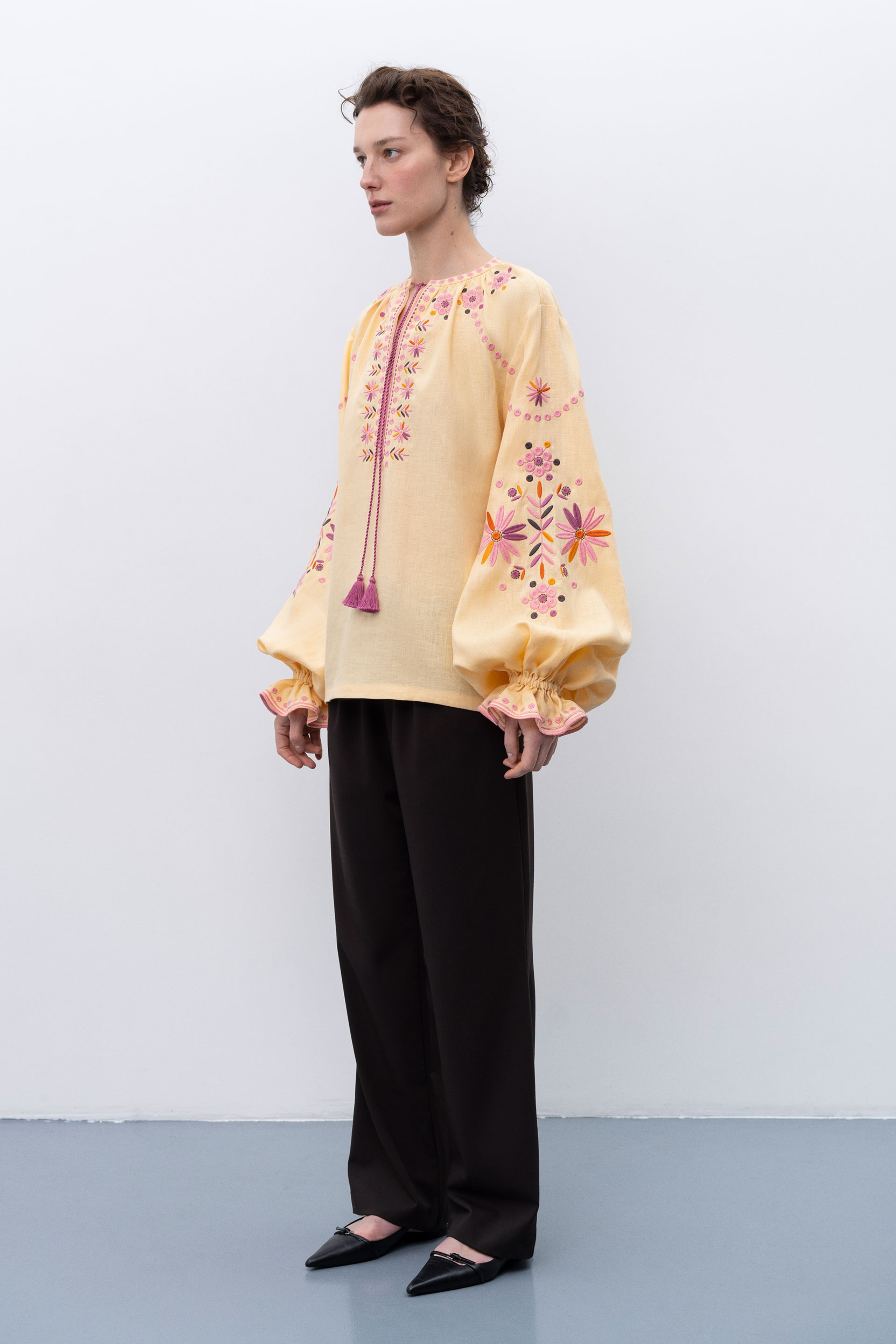 Woman wearing a yellow embroidered blouse with black pants against a white background