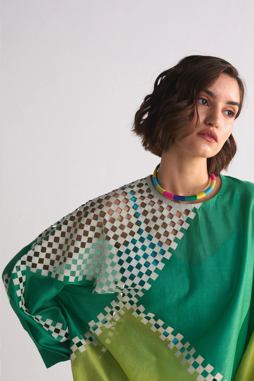 Woman wearing a green and patterned top against a white background