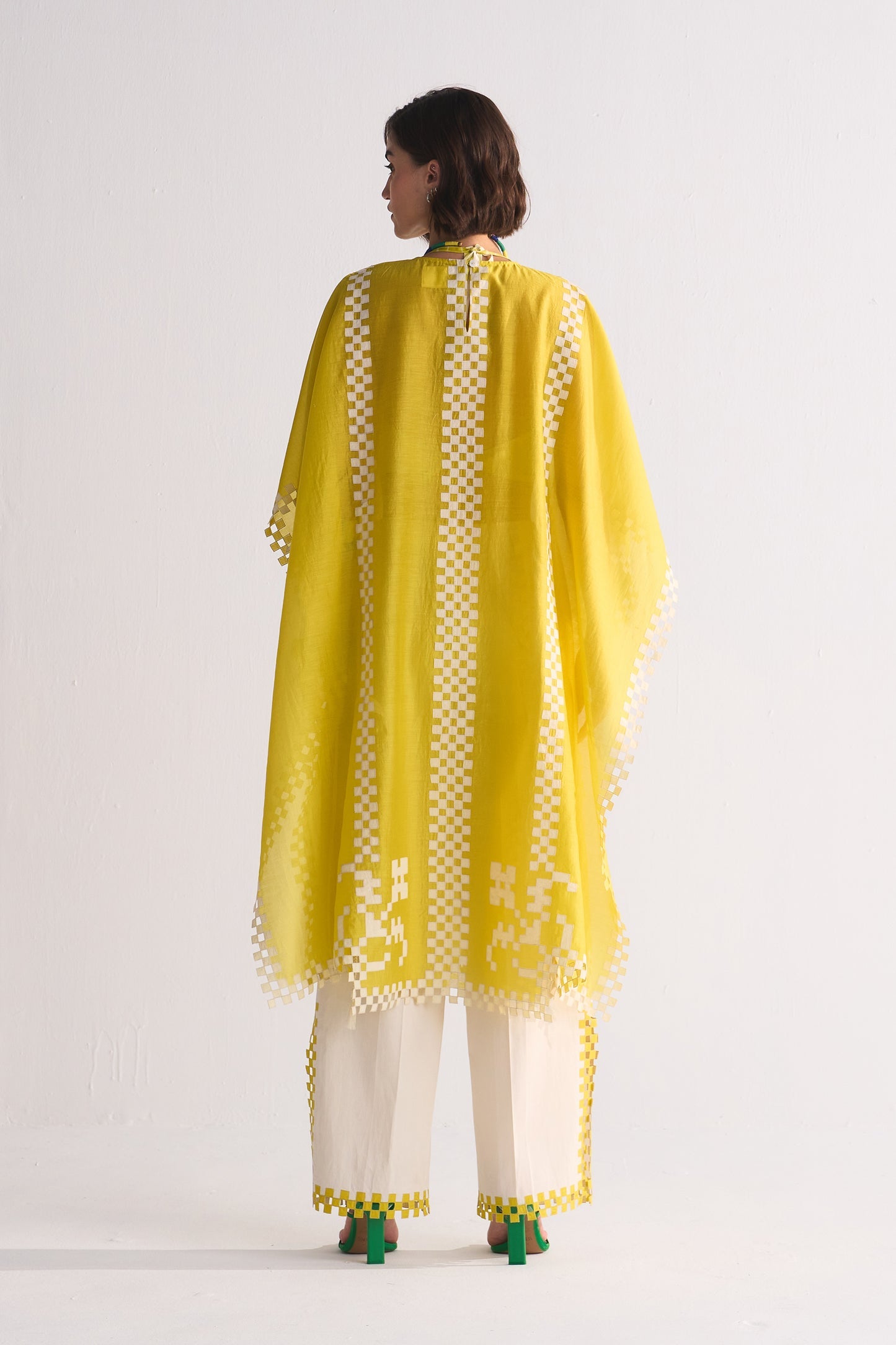 Woman wearing a yellow embroidered traditional outfit with white pants on a light gray background