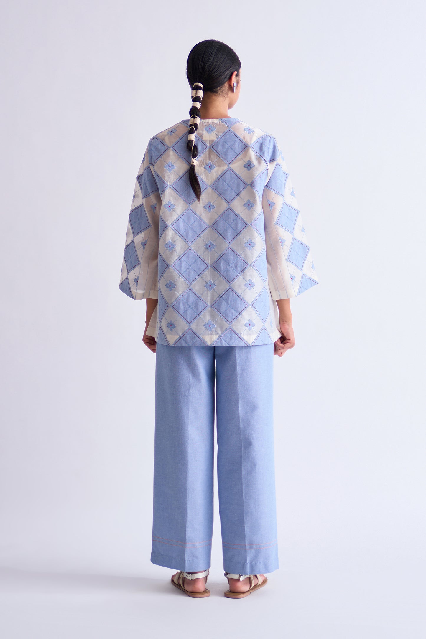 Person wearing a light blue and white patterned top with wide-leg pants on a white background