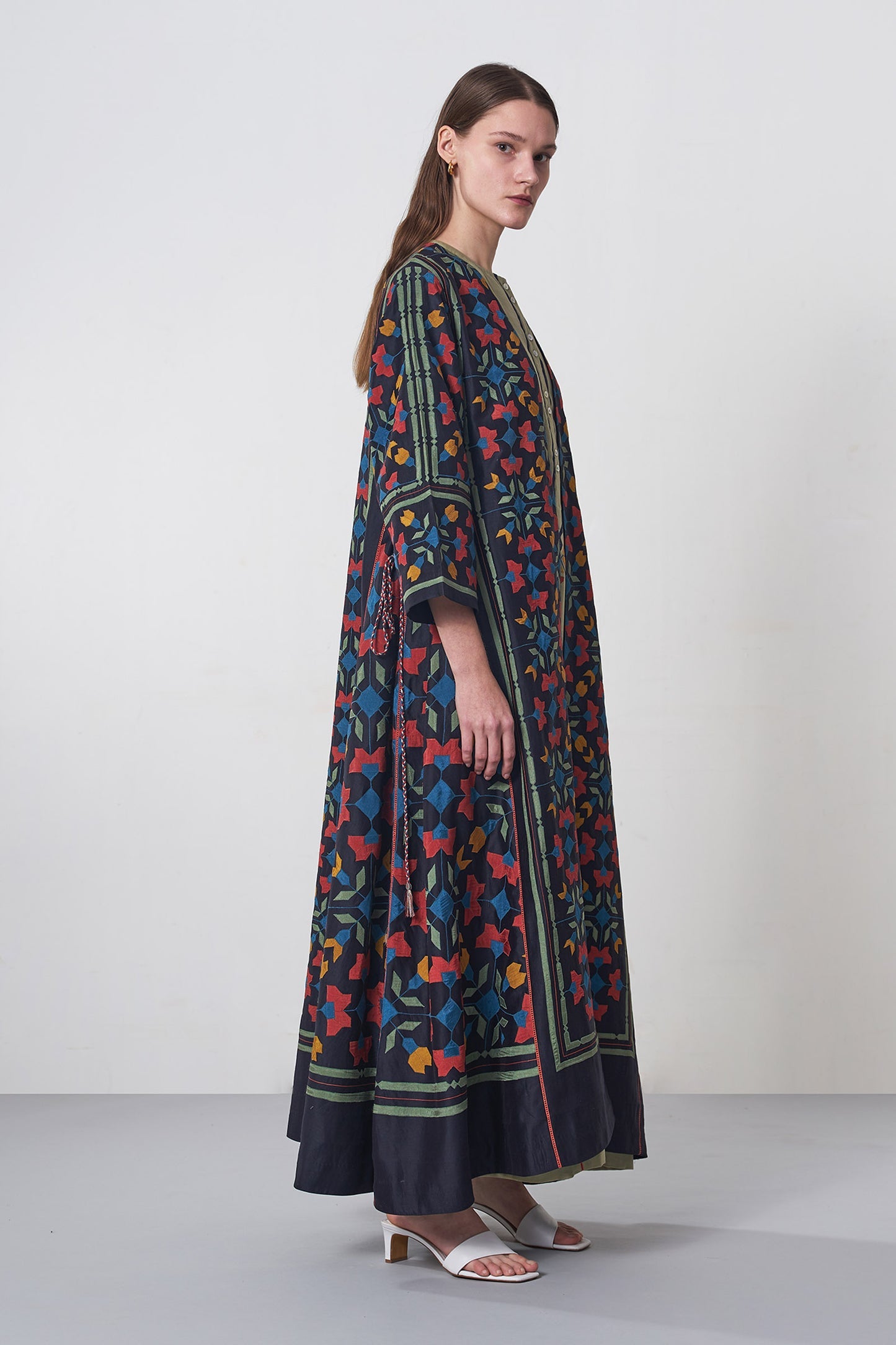 Woman wearing a long, patterned dress against a plain background