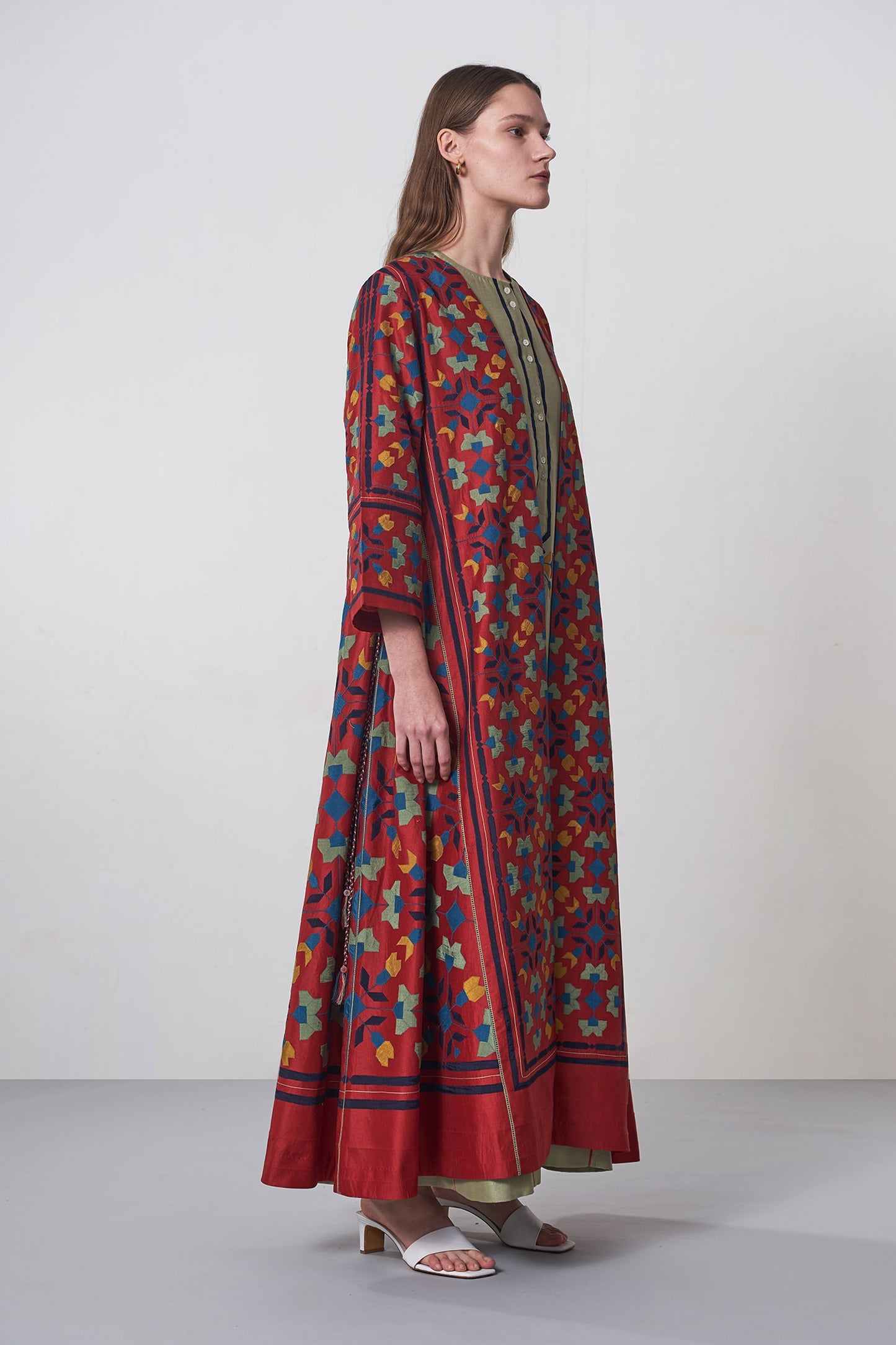 Woman wearing a long, patterned dress with a colorful design on a plain background