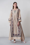 Woman wearing a long beige embroidered dress on a plain background