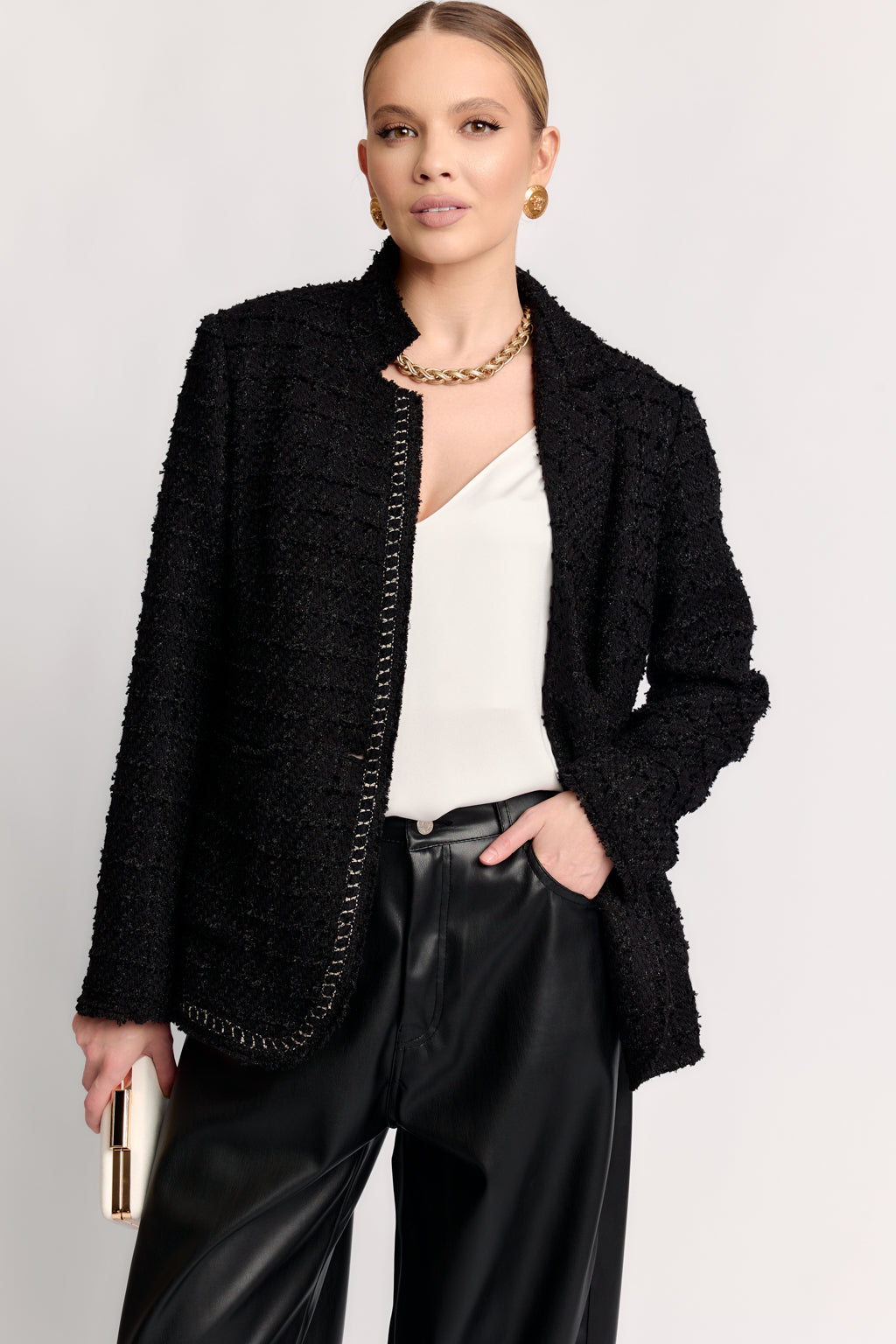 Woman wearing a black textured jacket over a white top and black pants on a light gray background