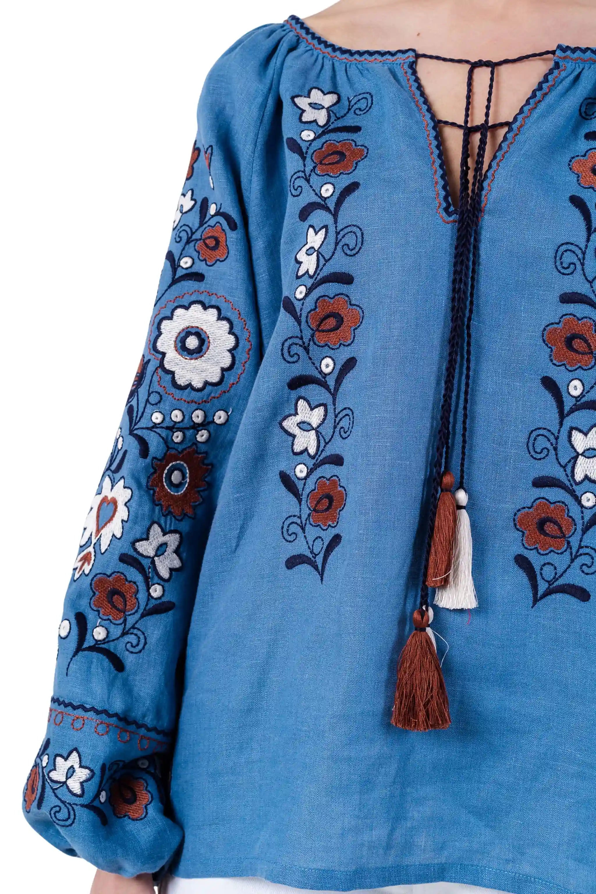 A close-up of a blue embroidered blouse with floral patterns in brown, white, and navy, featuring a lace-up V-neckline with tassel ties.