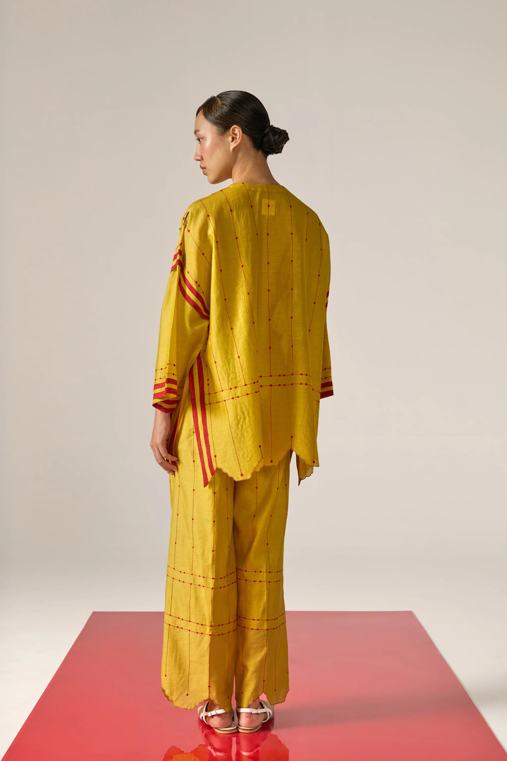 A  woman model wearing yellow Cotton Silk Chanderi kaftan shirt with teal geometric appliqué and cutwork detailing on the sleeves and back, paired with matching trousers.
