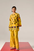 A  woman model wearing yellow Cotton Silk Chanderi kaftan shirt with teal geometric appliqué and cutwork detailing on the sleeves and back, paired with matching trousers.