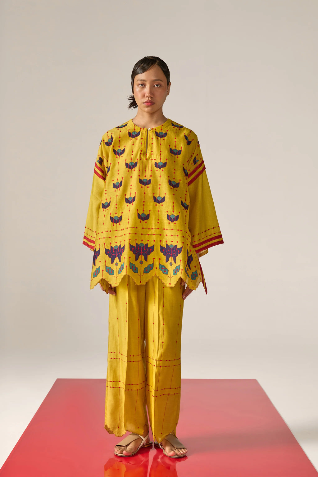 A  woman model wearing yellow Cotton Silk Chanderi kaftan shirt with teal geometric appliqué and cutwork detailing on the sleeves and back, paired with matching trousers.