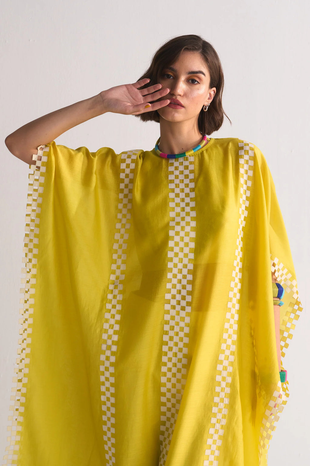A model wearing a vibrant yellow free-size kaftan with intricate white geometric cutwork and appliqué patterns along the borders and central panels.