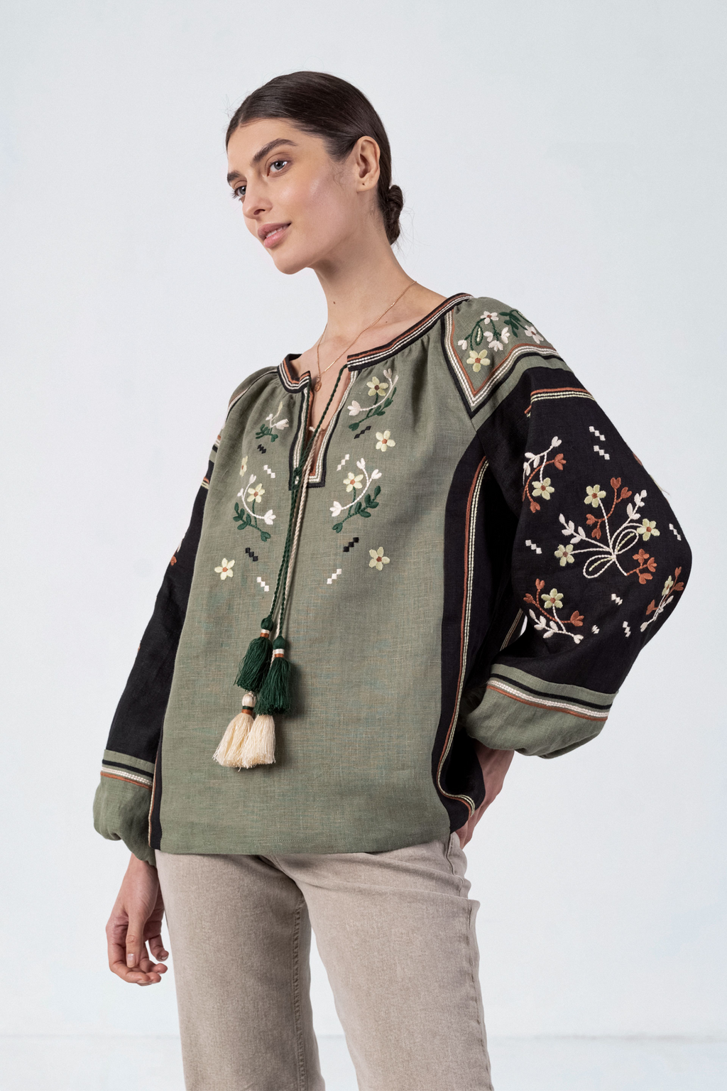 Woman wearing a green embroidered blouse with tassels on a white background