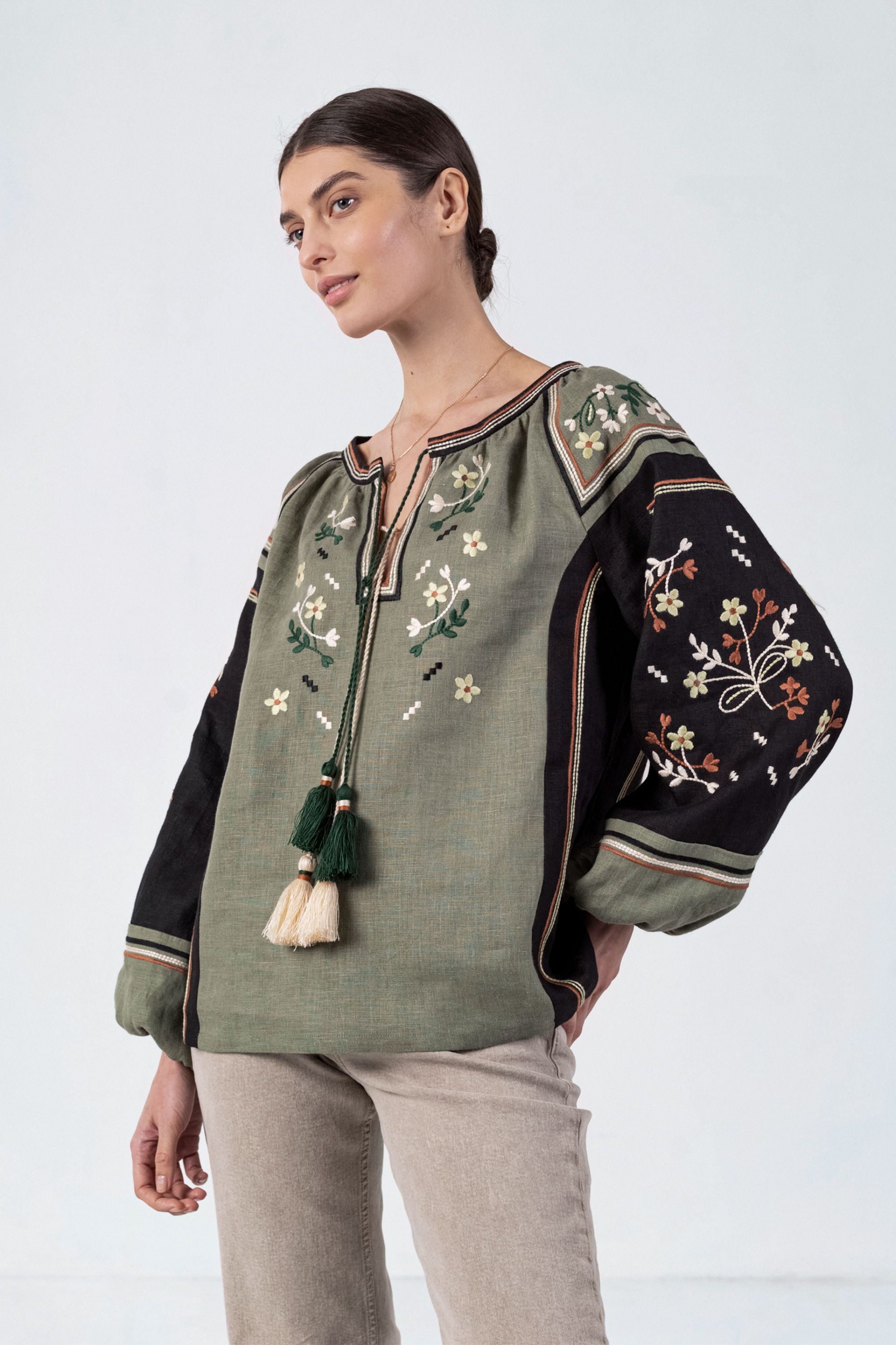Woman wearing a green embroidered blouse with tassels on a white background