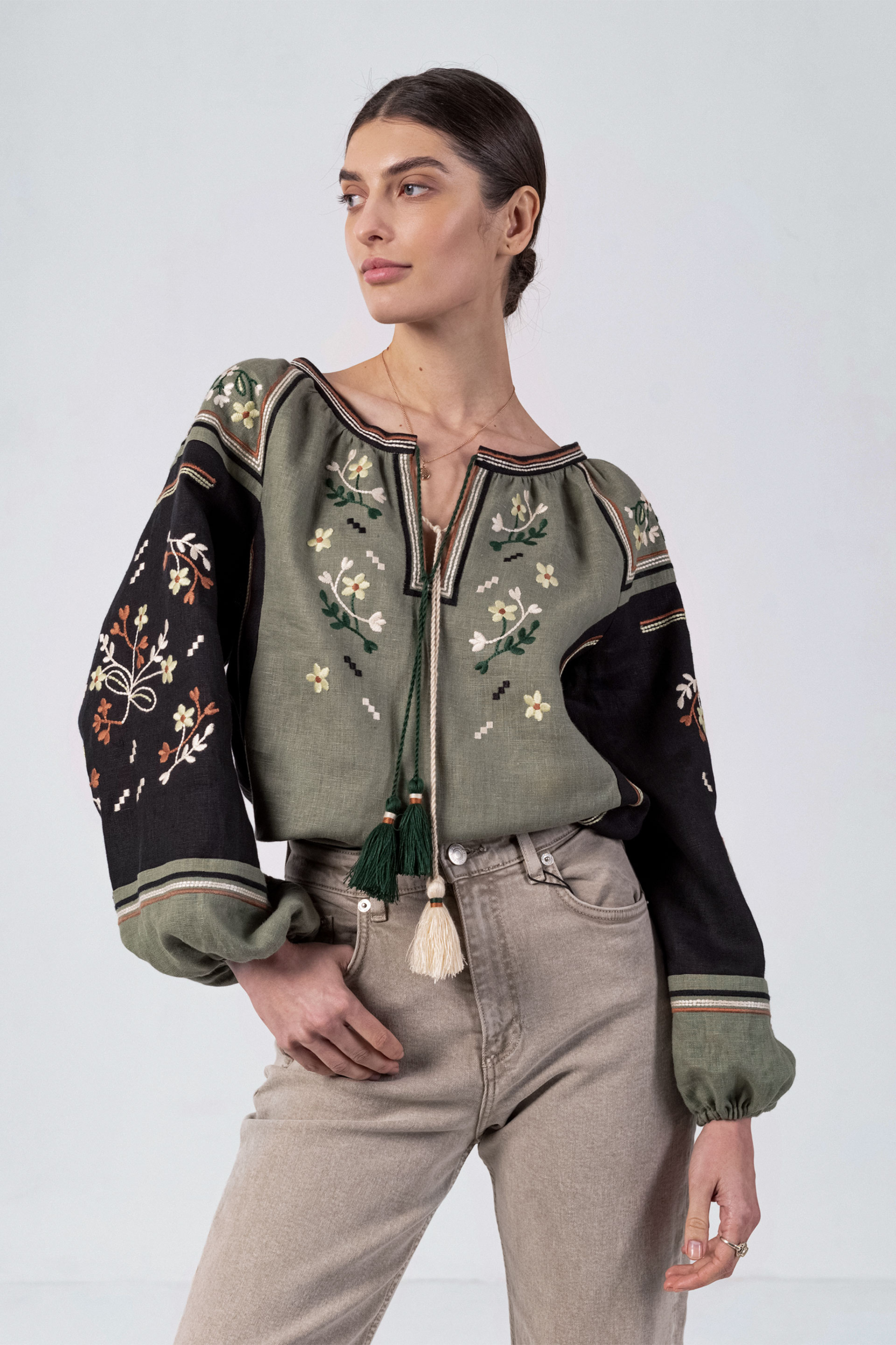 Woman wearing a green embroidered jacket with black sleeves on a white background