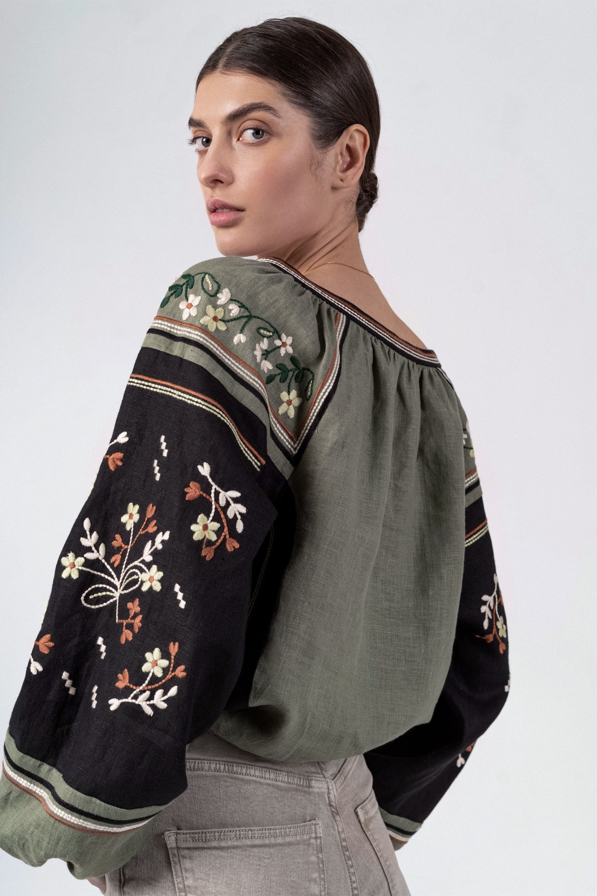 Woman wearing a green embroidered blouse with tassels on a white 