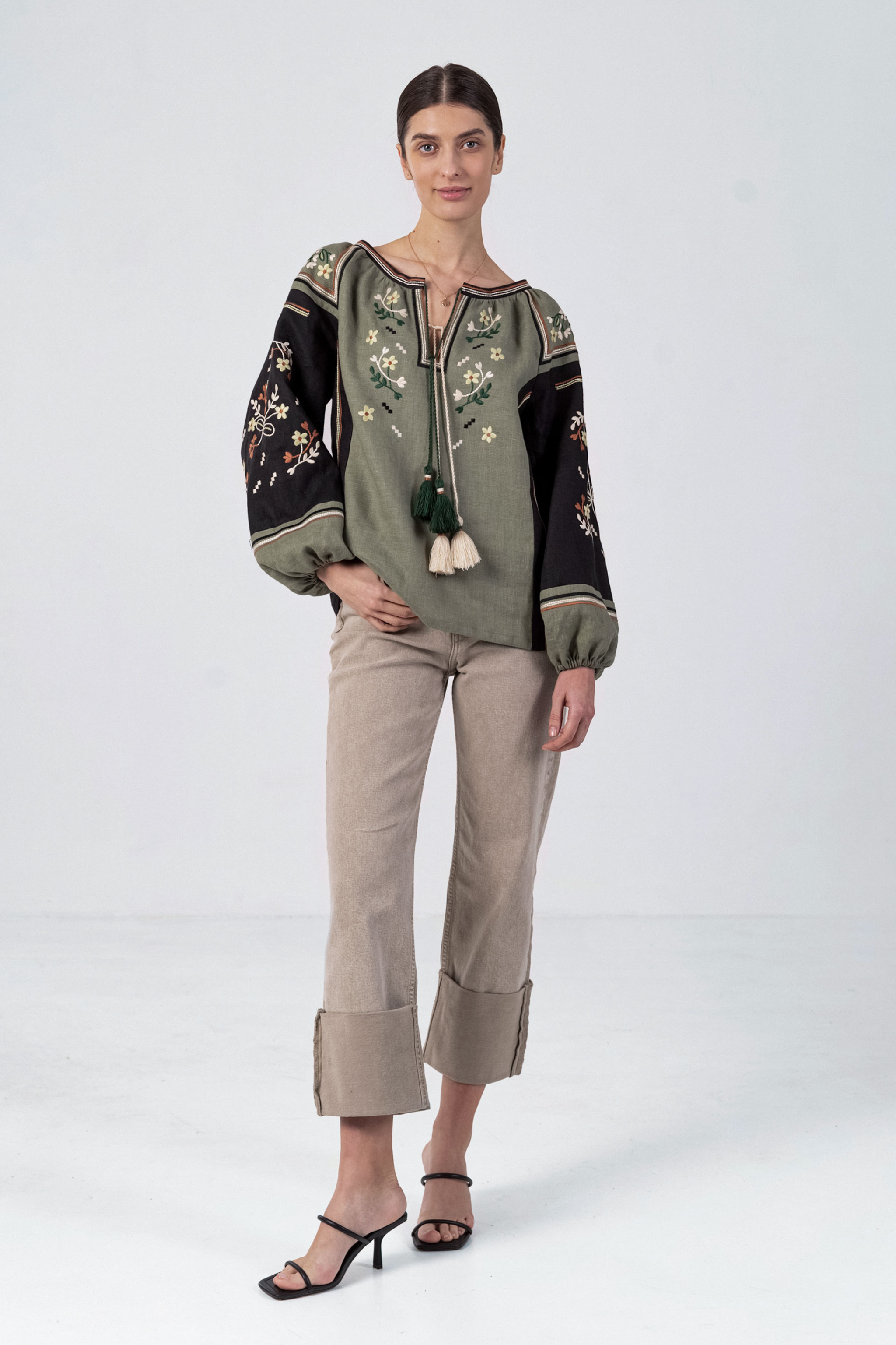 Woman wearing a green embroidered blouse with tassels on a white 