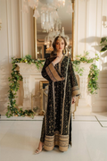 Woman in a black and gold traditional outfit standing in an elegant room with decorative elements.