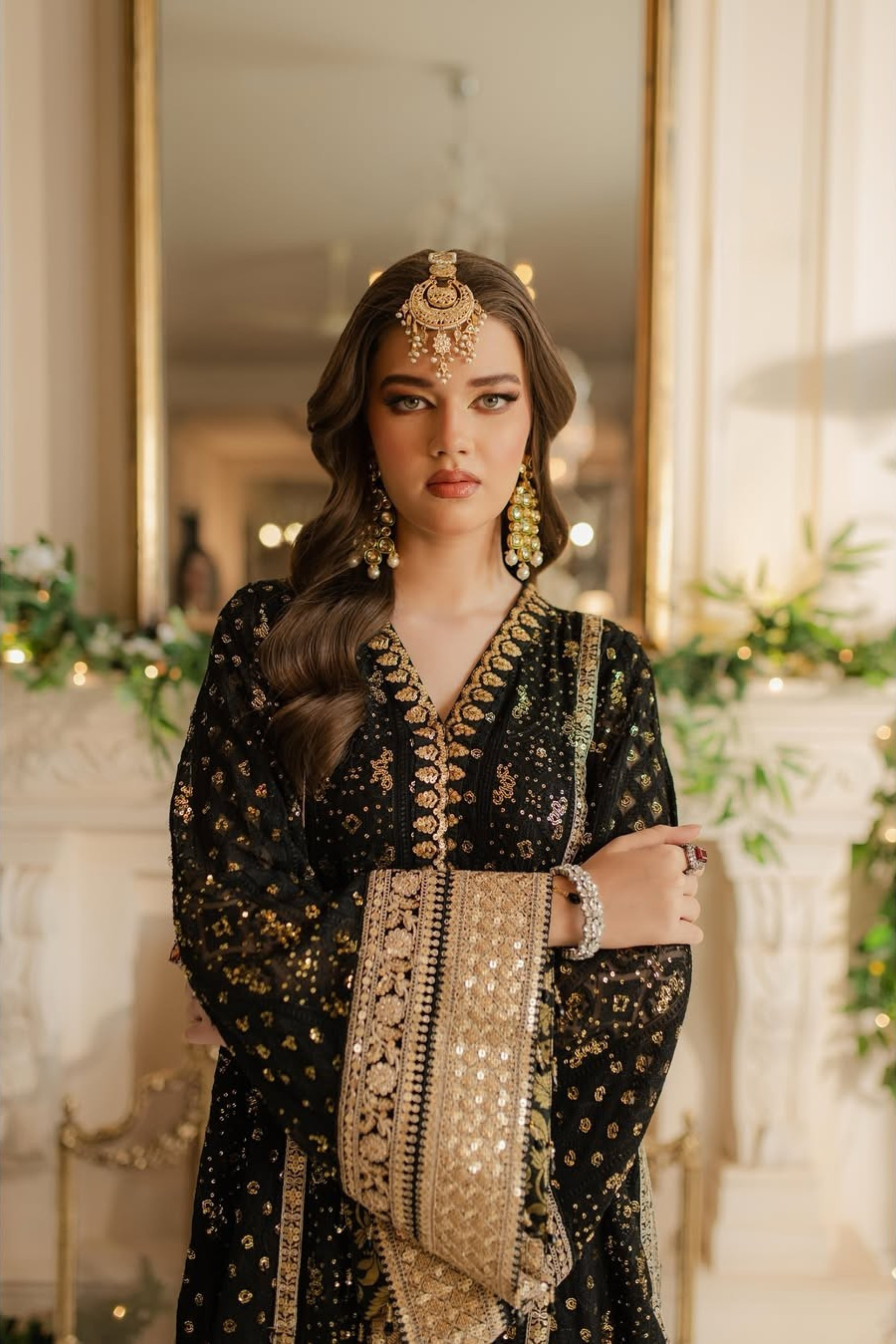 Woman in traditional black and gold embroidered outfit with jewelry in a decorated indoor setting